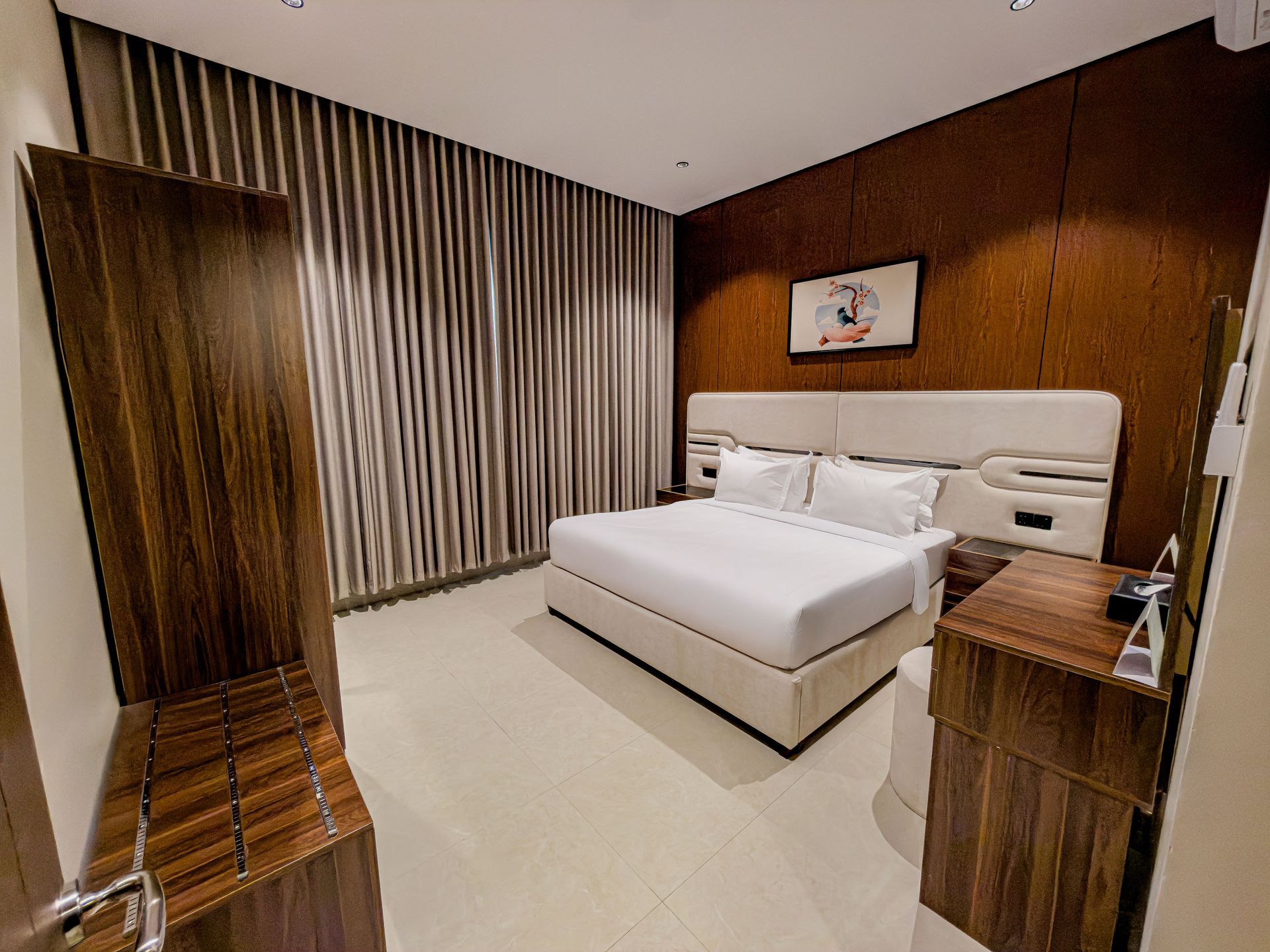 A modern hotel room with a queen bed, dark wood accent wall, wooden luggage rack, and floor-to-ceiling striped curtains.