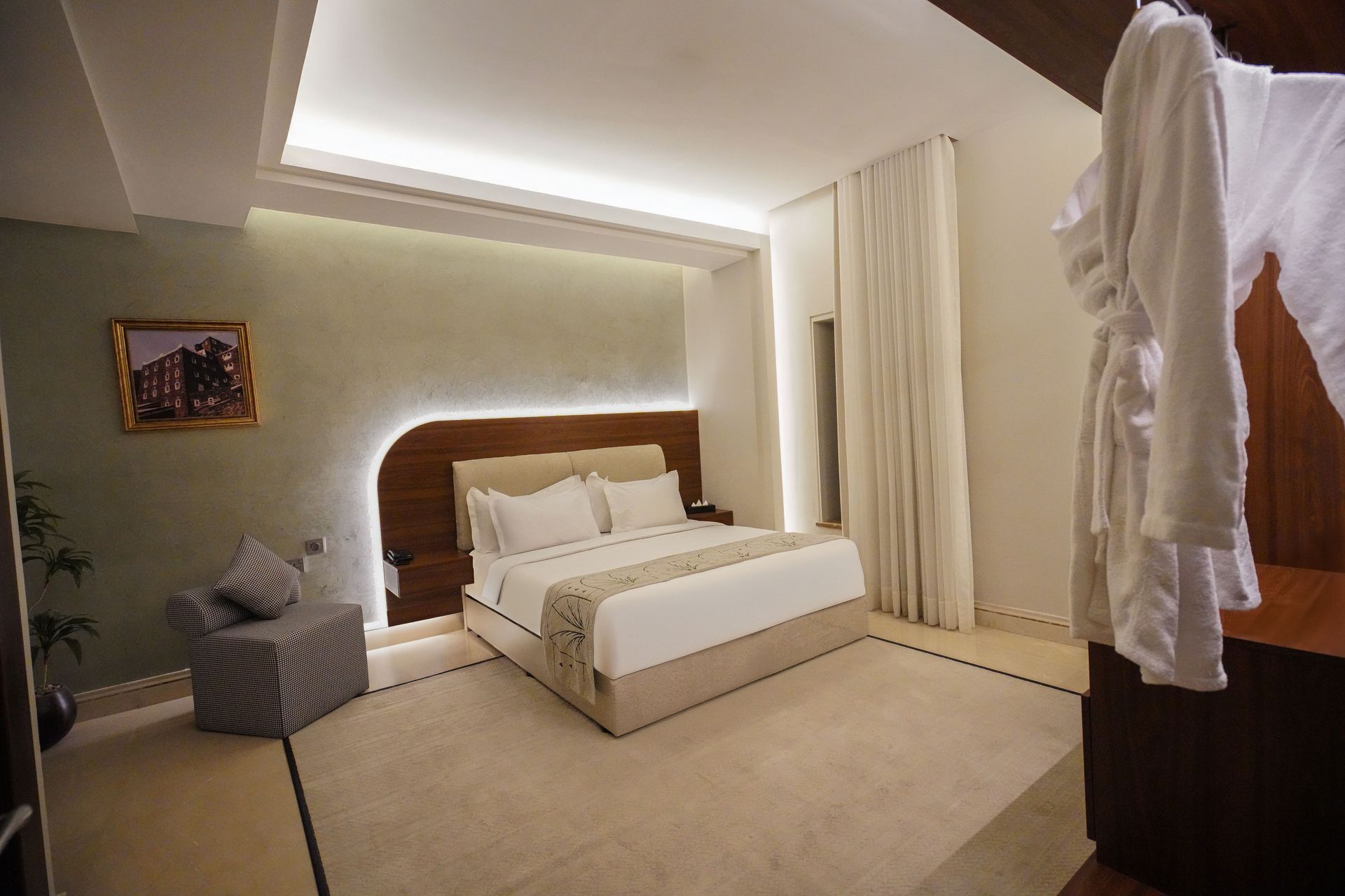 Modern beige bedroom with a large upholstered bed, curtains, chair, and warm recessed lighting