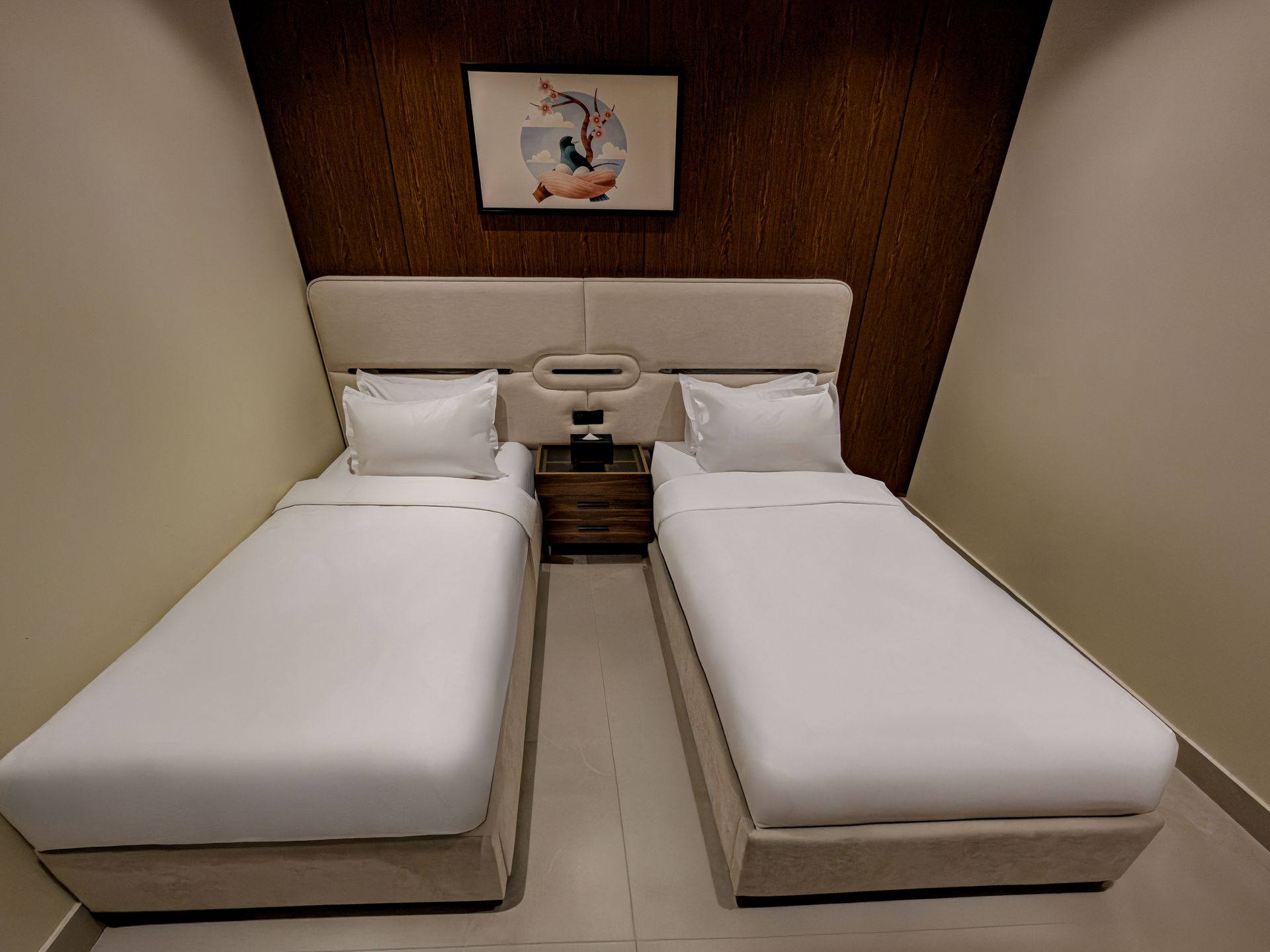 A hotel room with two twin beds featuring white bedding, a shared wooden nightstand, and framed artwork on the wall.