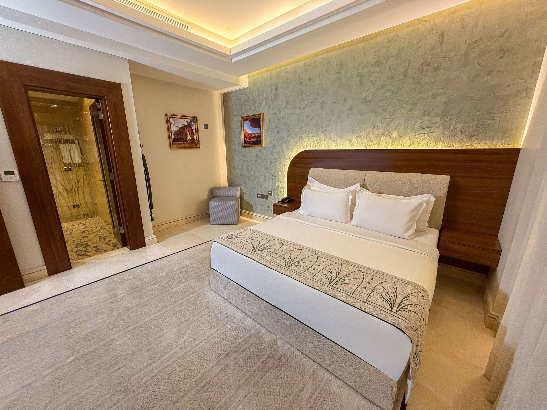 Modern hotel bedroom with king bed, wood headboard, soft lighting, and beige decor