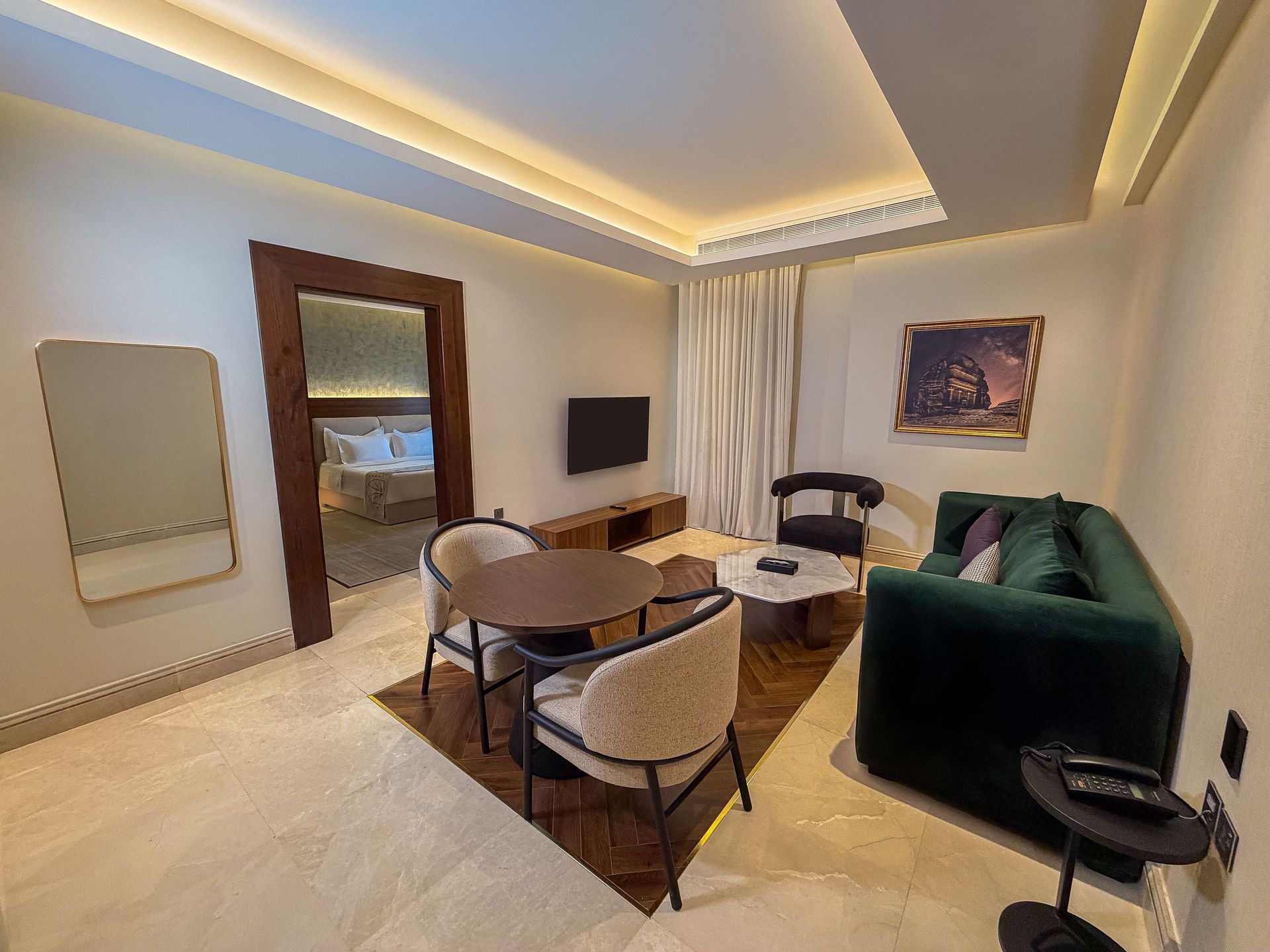 Modern living room with green sofa, round dining table, TV, and warm recessed lighting