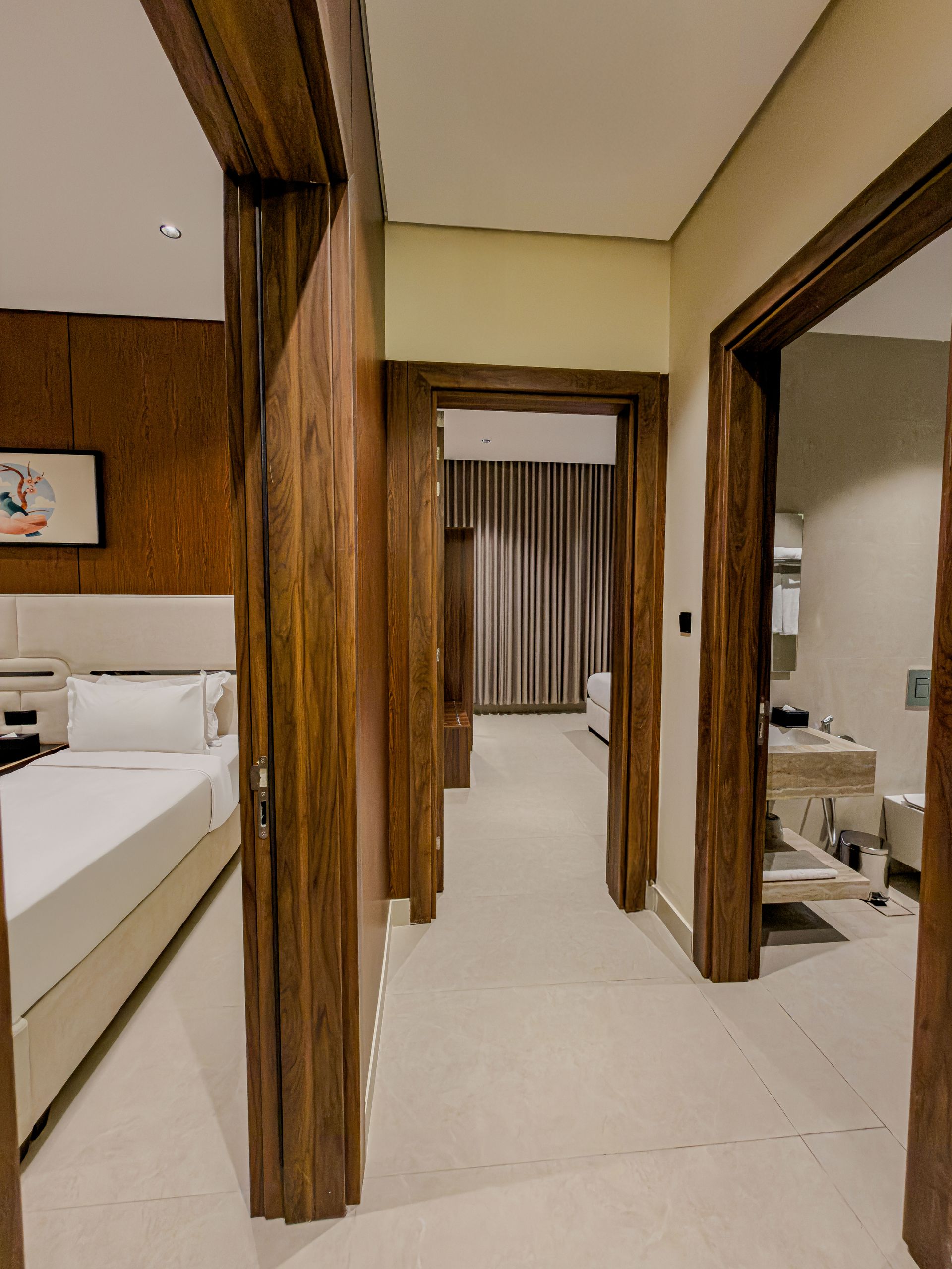 A hallway view showing a bedroom on the left, an open doorway leading to a room in the back, and a bathroom on the right.
