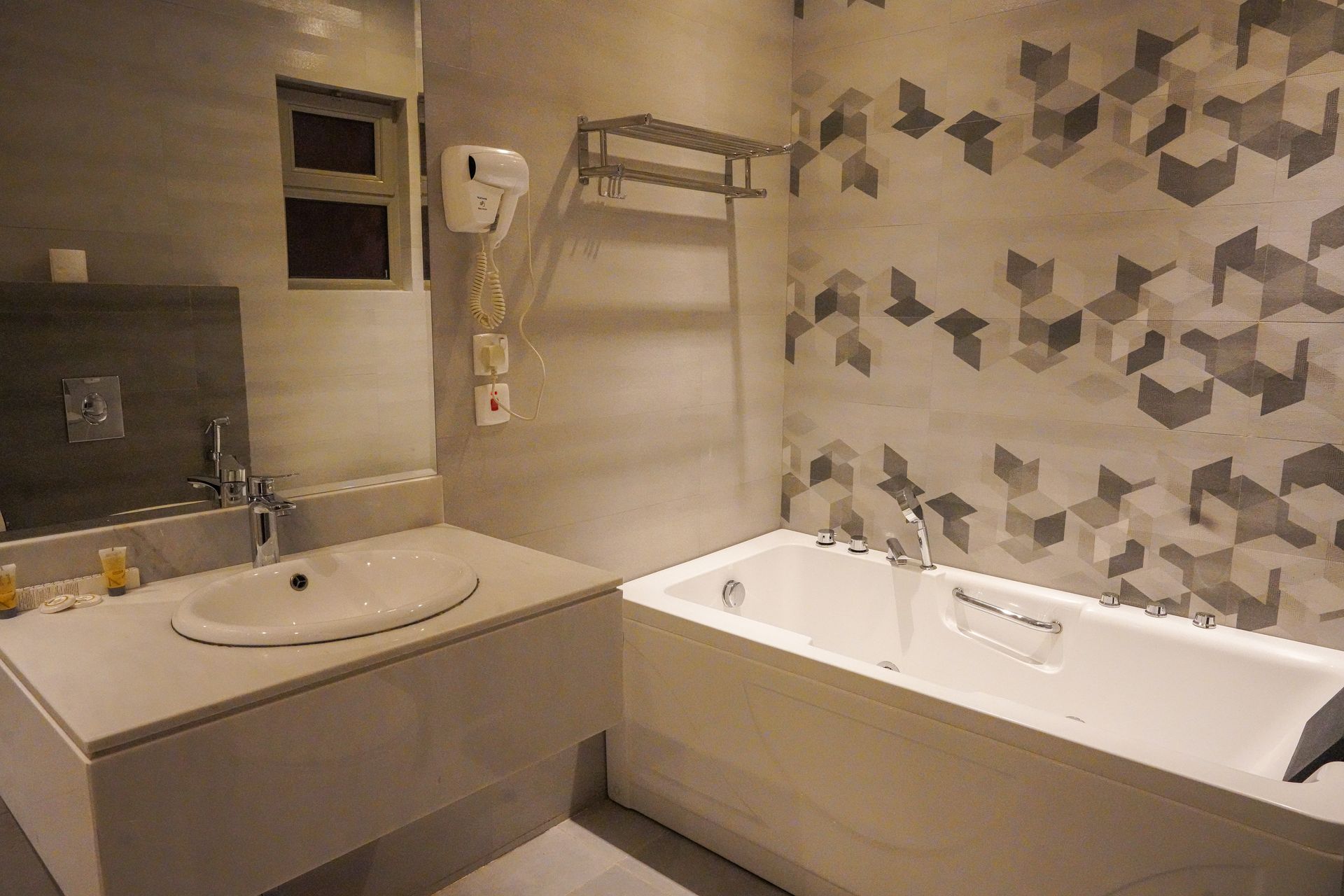 Modern bathroom with sink, mirror, towel rack, and white bathtub with patterned tile wall.