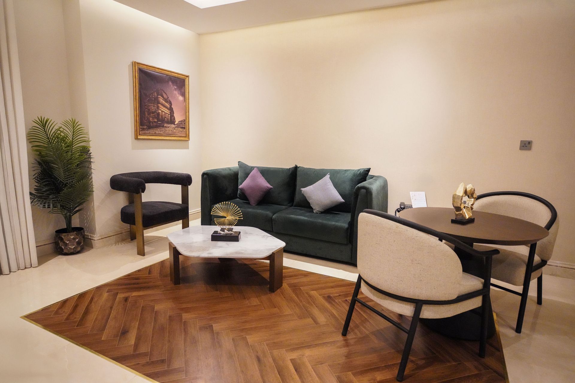 Modern living room with green sofa, round dining table, coffee table, and herringbone wooden floor.
