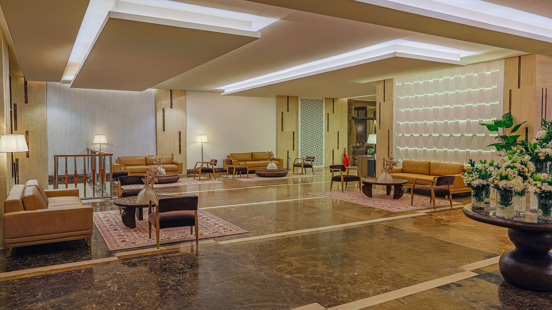 A modern hotel lobby featuring beige leather seating, patterned rugs, marble floors, and soft, recessed lighting.
