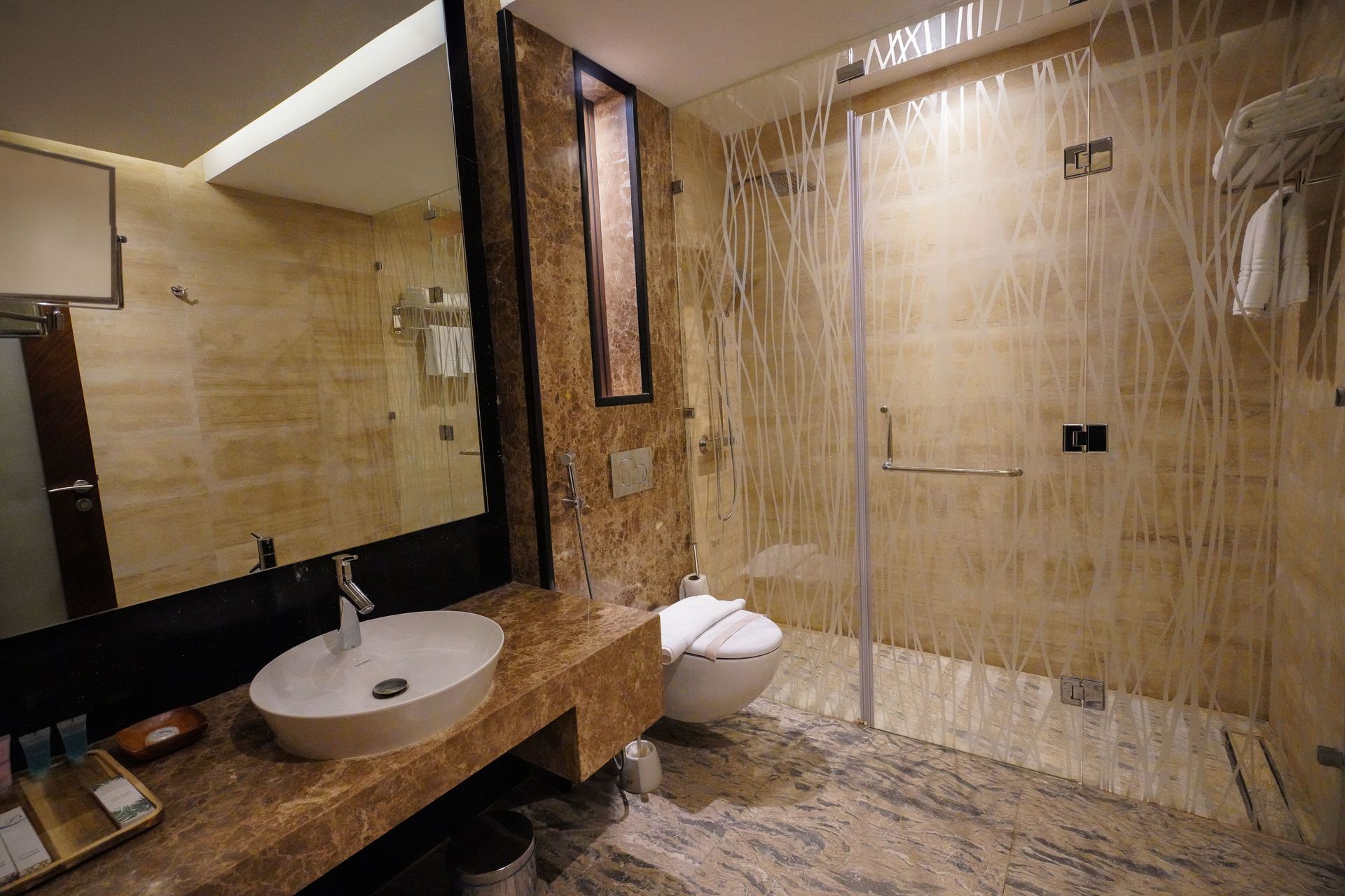 Modern bathroom with marble tile, glass shower, sink, mirror, and toilet