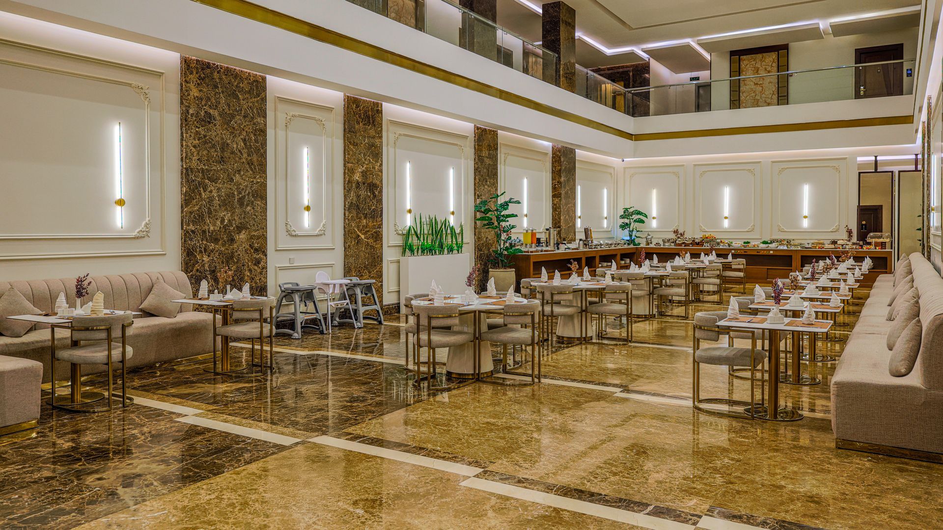 A spacious, luxury restaurant dining room with marble floors, beige seating, and warm, minimalist wall lighting.