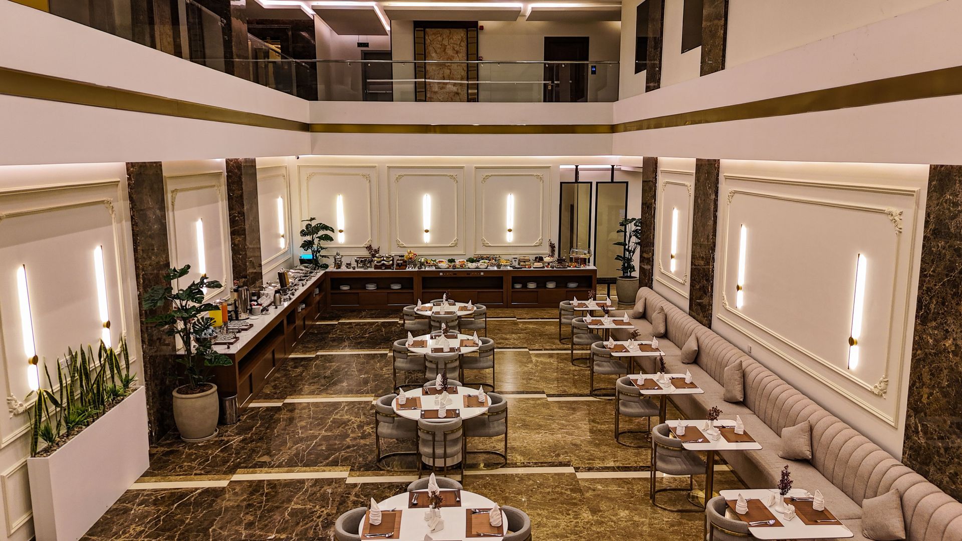 Elegant hotel restaurant with tables, booth seating, marble floors, and vertical wall lights in a modern dining hall.