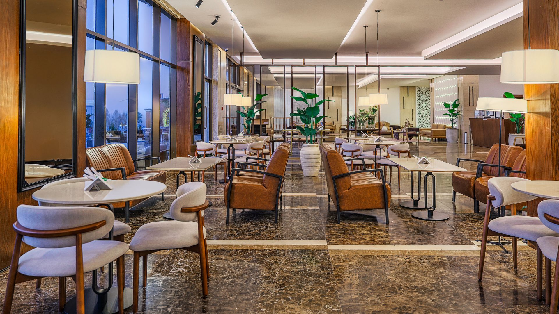 Modern restaurant dining area with tables and chairs, large floor-to-ceiling windows, and warm ambient lighting.