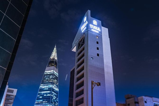 Tall, illuminated hexagonal skyscraper at night, with palm trees and soft lighting at the base.