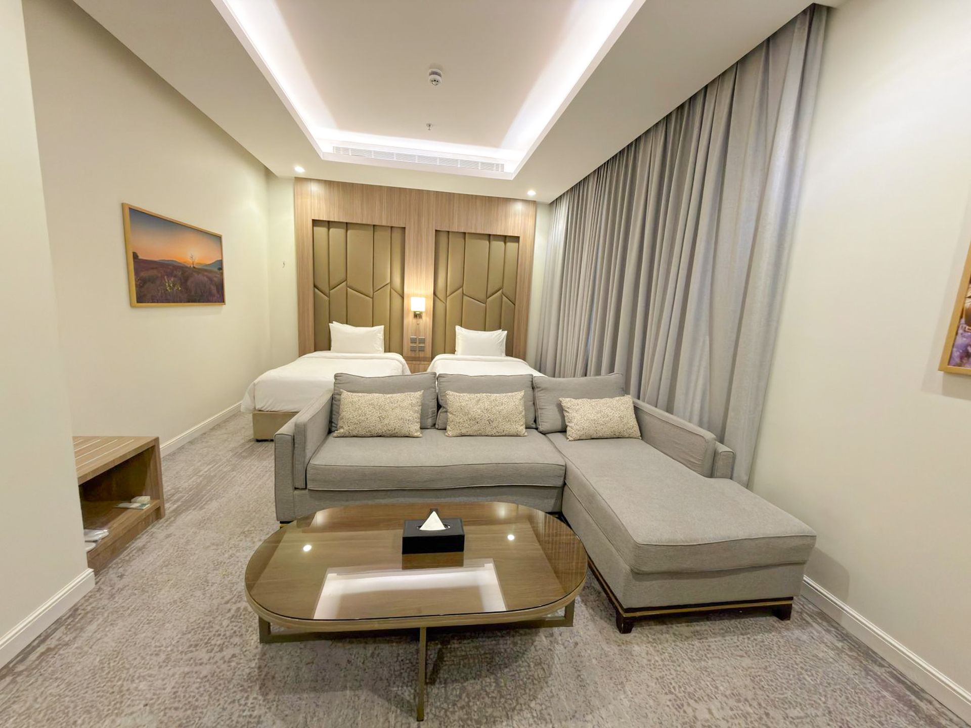 Modern living room with gray sectional sofa, glass coffee table, and soft ceiling lighting