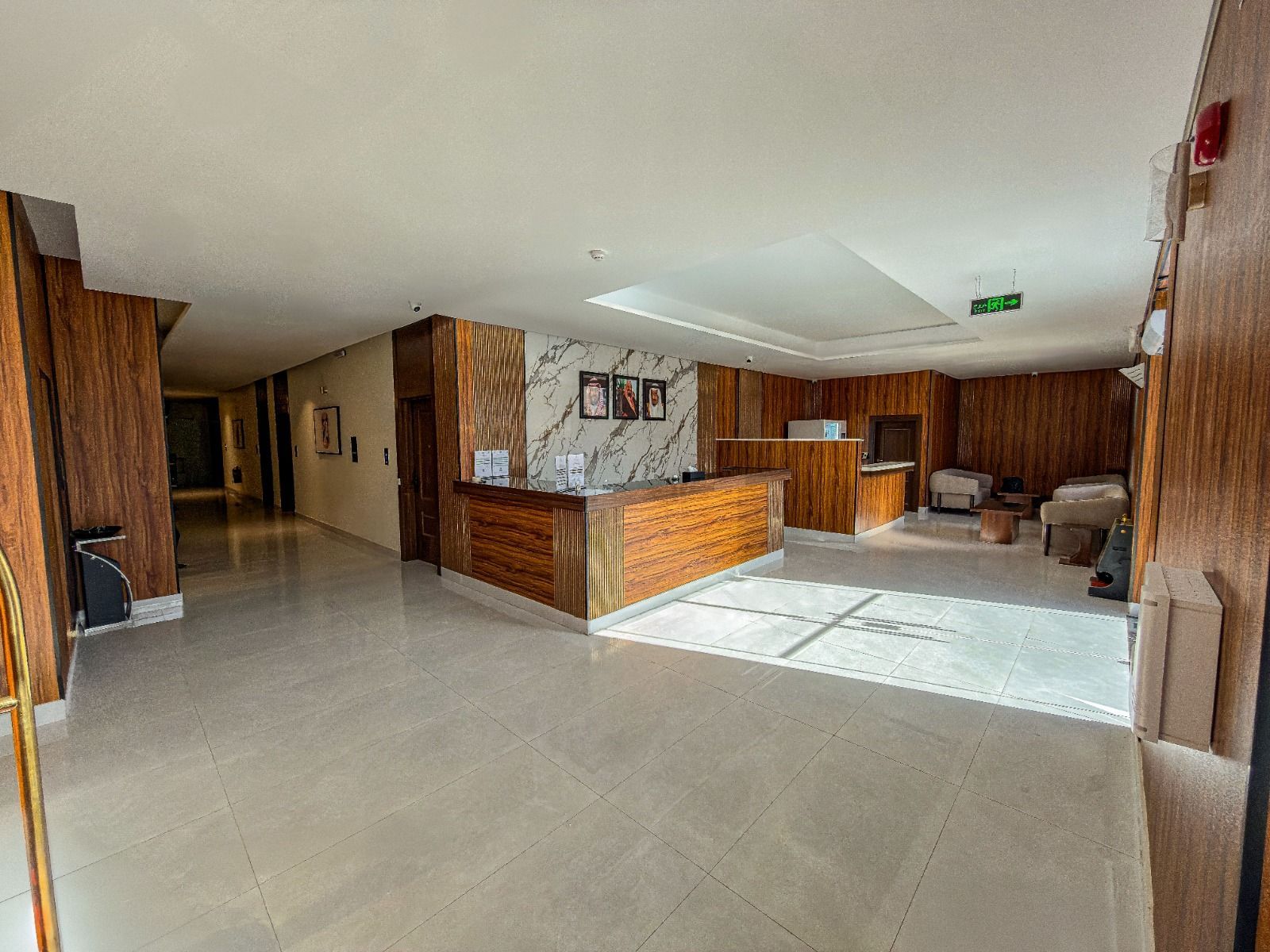 Hotel lobby with a wooden reception desk, marble floors, and decorative wall portraits on a white, patterned background.