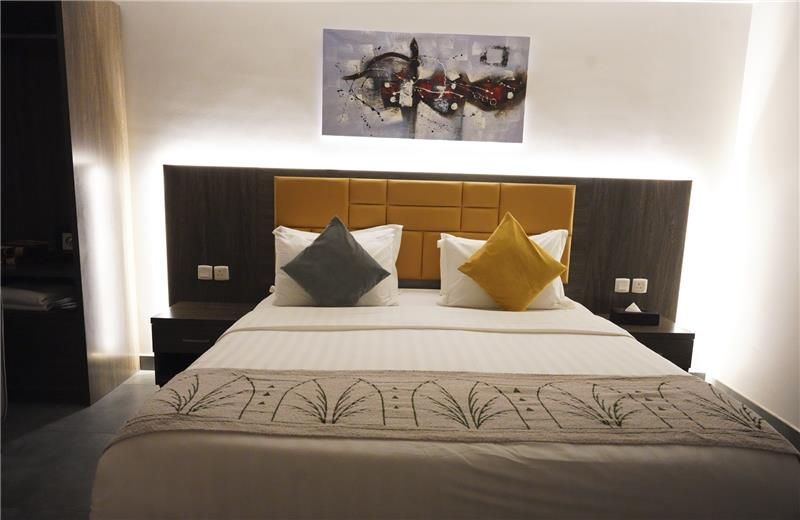 Modern hotel bedroom with a neatly made bed, gray and yellow pillows, and wall art above the headboard
