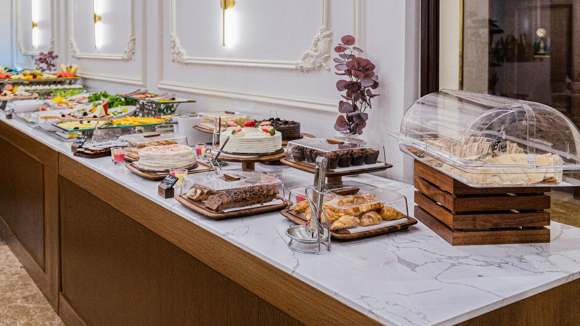 A buffet table featuring a variety of cakes, pastries, and desserts arranged on a white marble counter.
