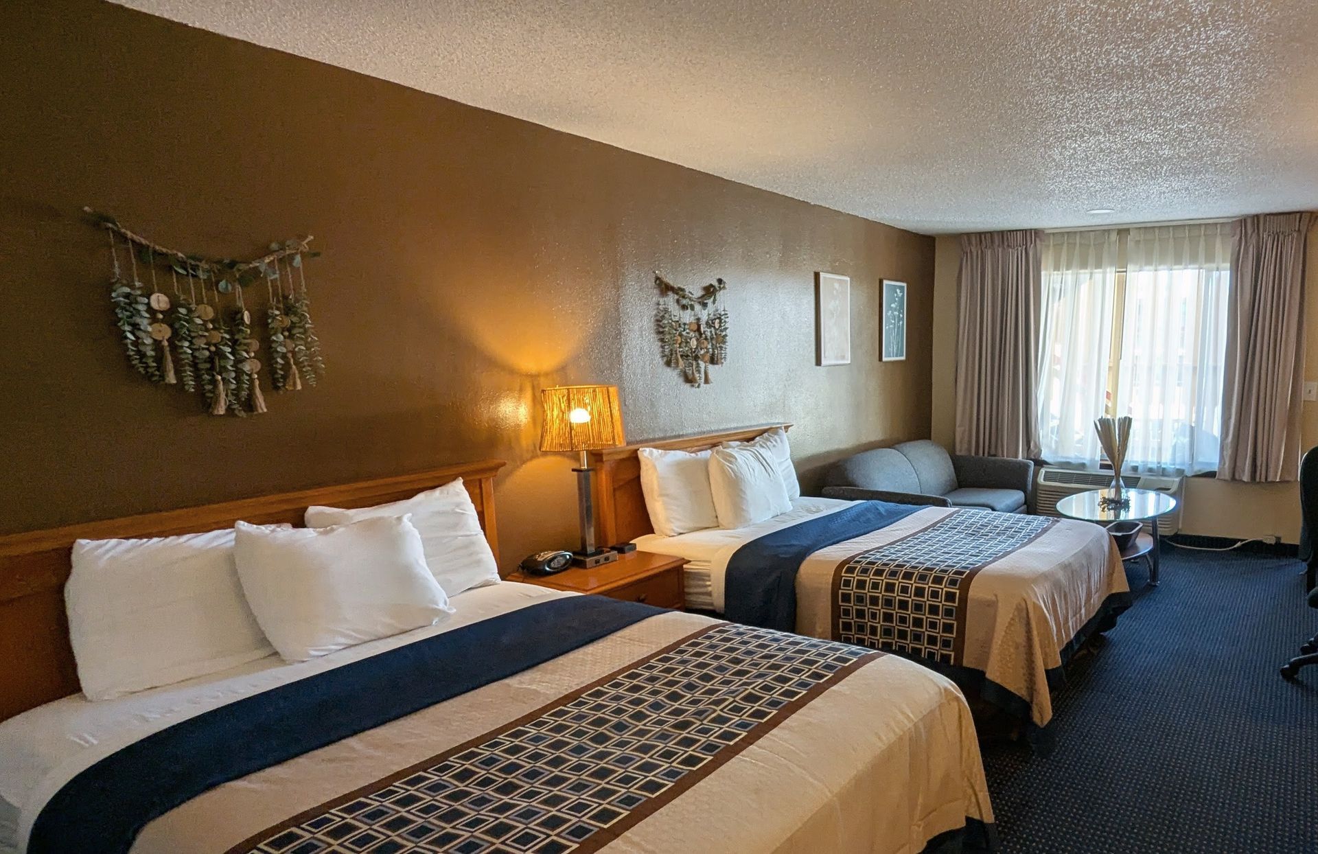 Hotel room with two neatly made beds, warm lamps, and a window with curtains.