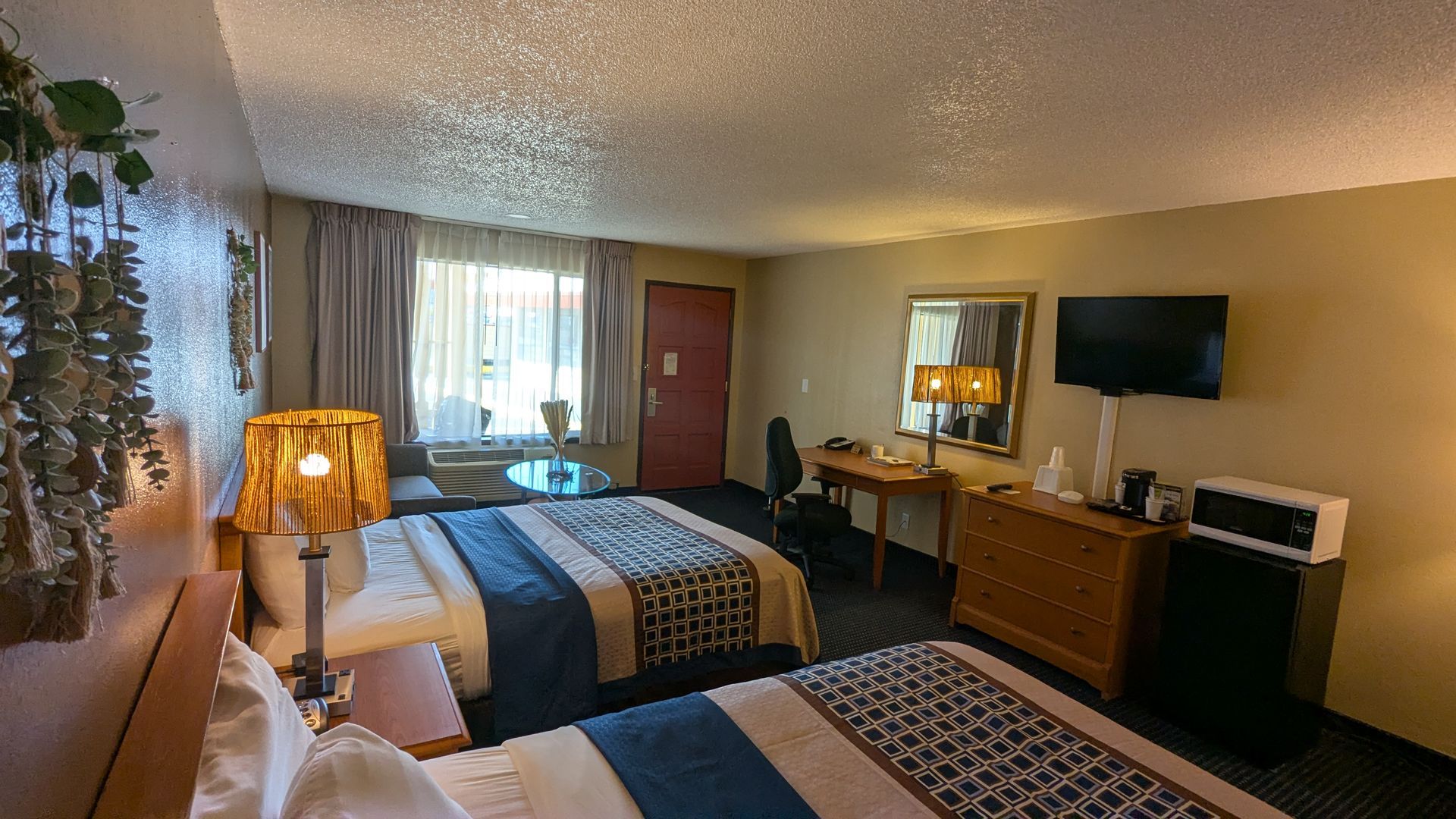 Motel room with two beds, a window, dresser, TV, and warm lamps.