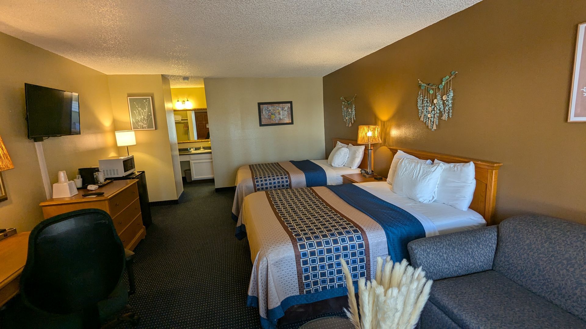 Hotel room with two beds, warm lighting, desk, TV, and wall art