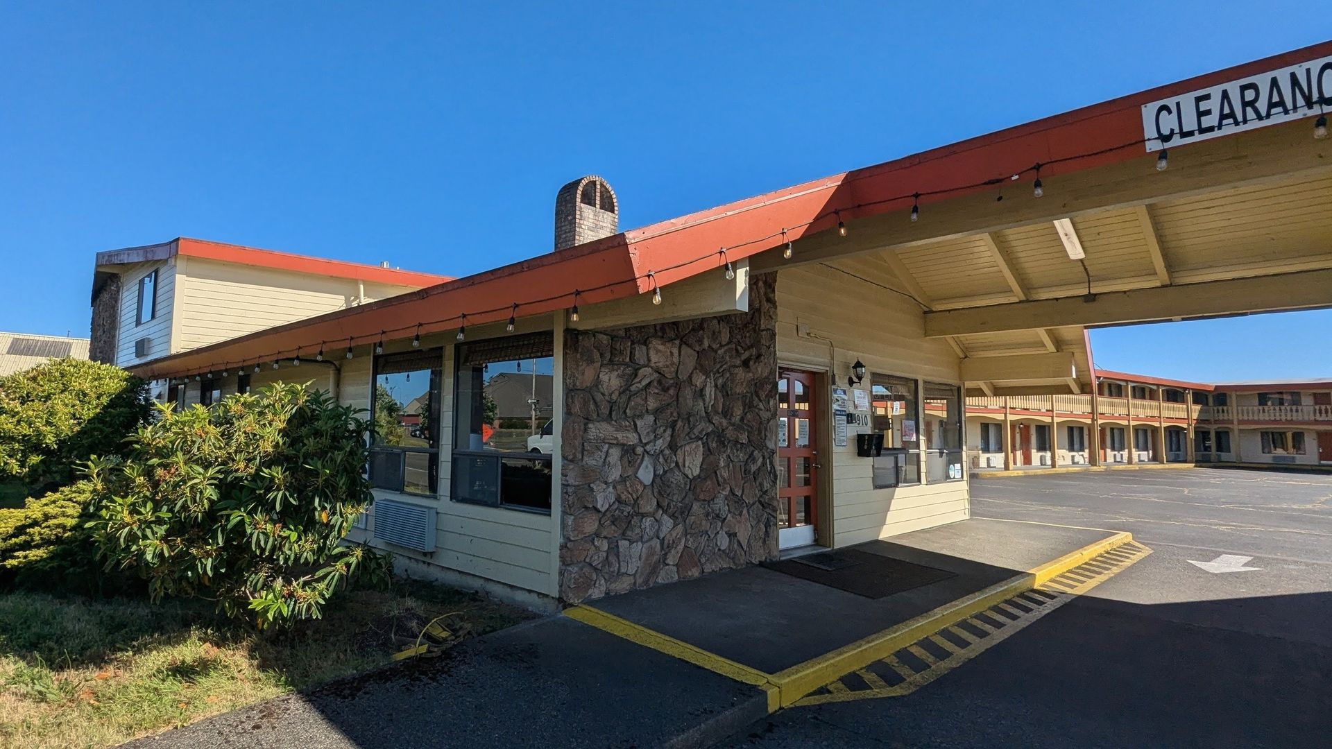 Two-story motel-style building beside a wide empty parking lot on a sunny day
