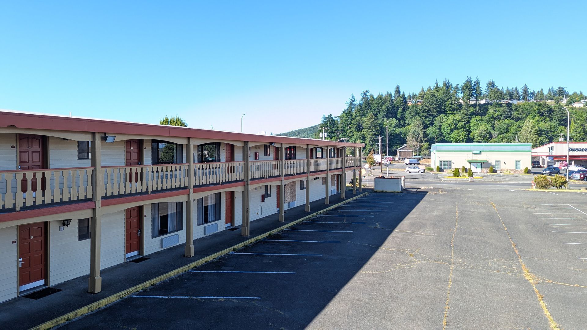Two-story motel-style building beside a wide empty parking lot on a sunny day