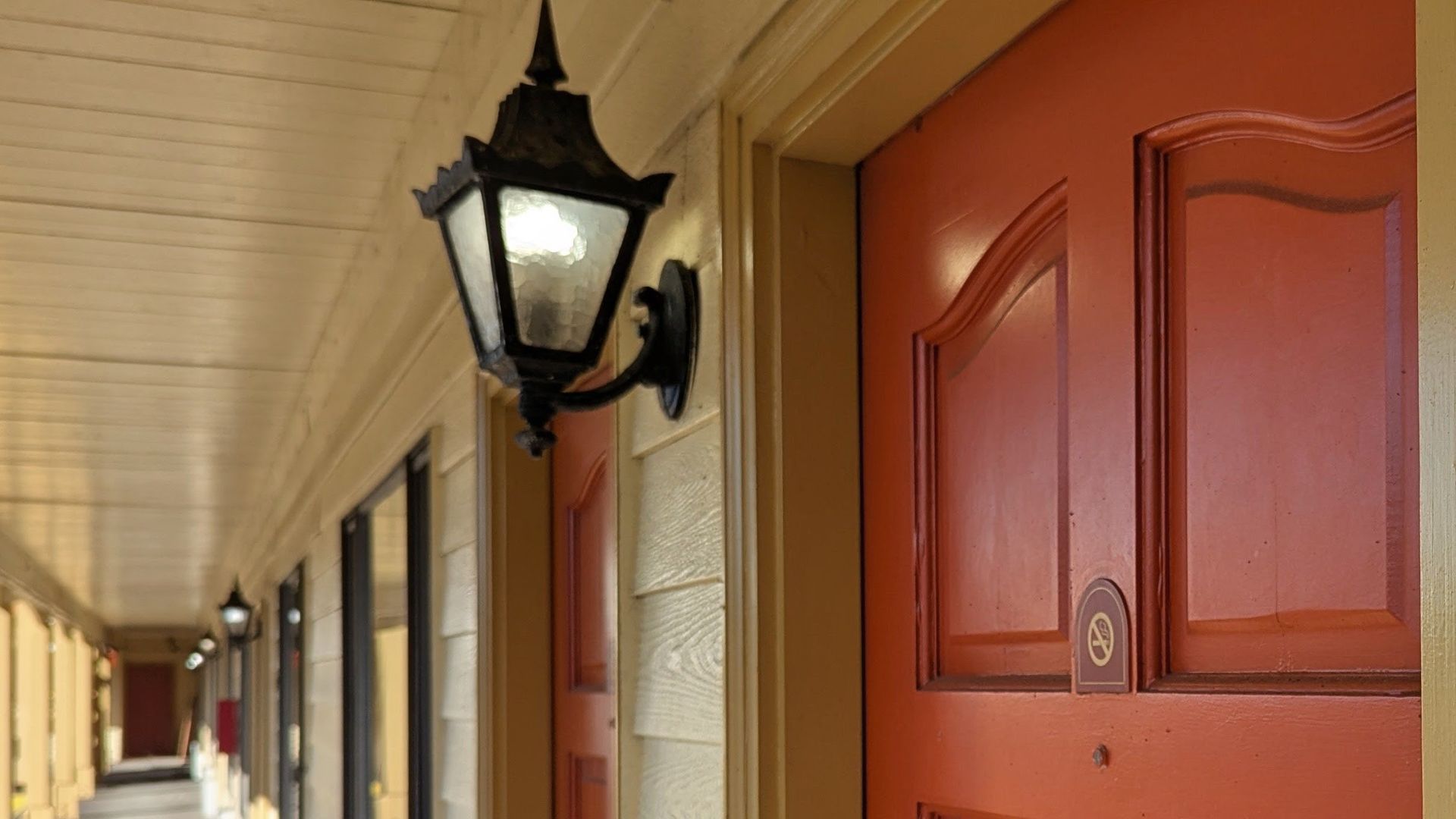 Covered porch with black lanterns and a red front door along cream siding