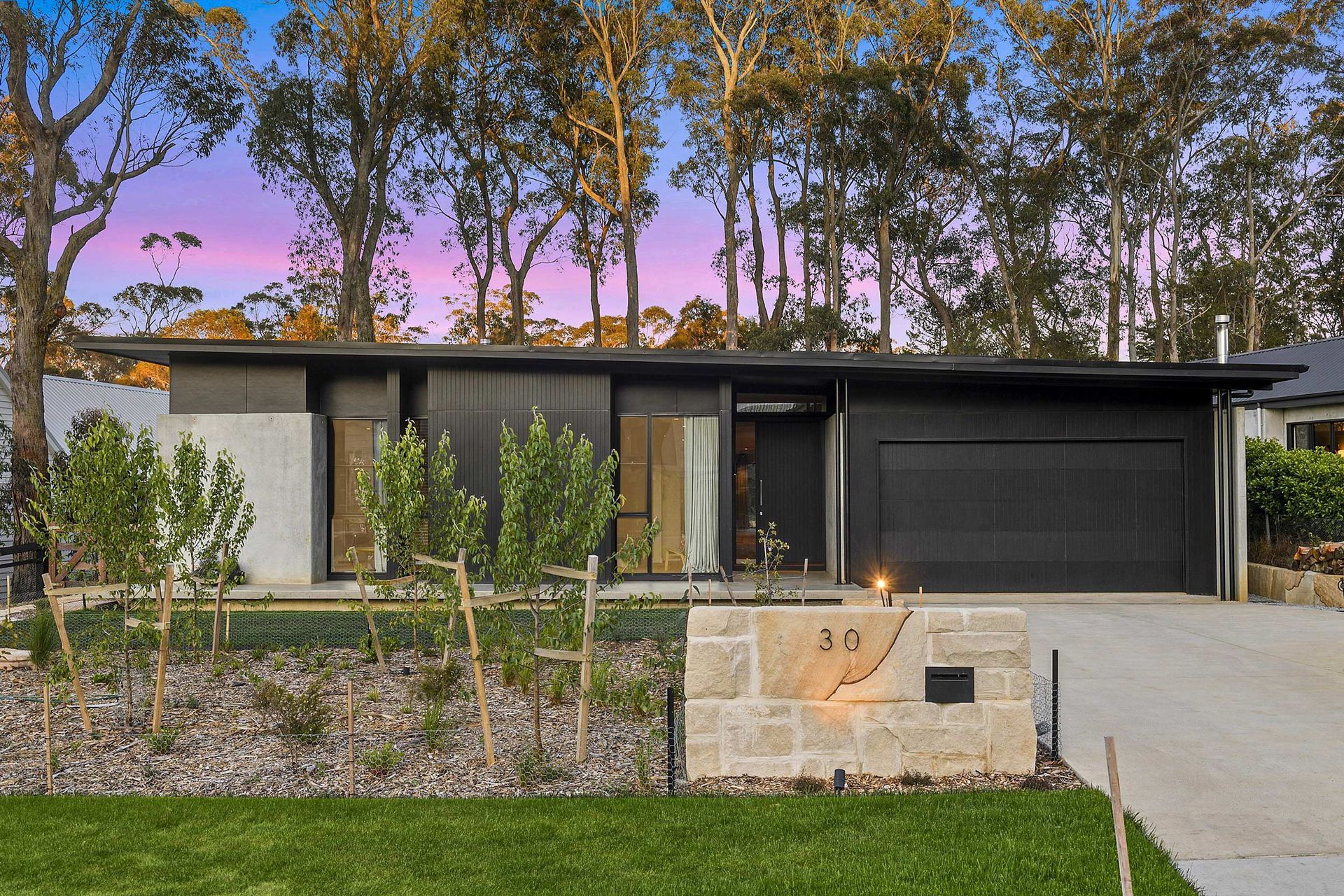 Trees surround a modern house with a black garage door.