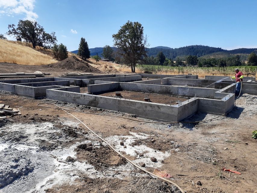 A man is standing in a dirt field next to a concrete foundation.