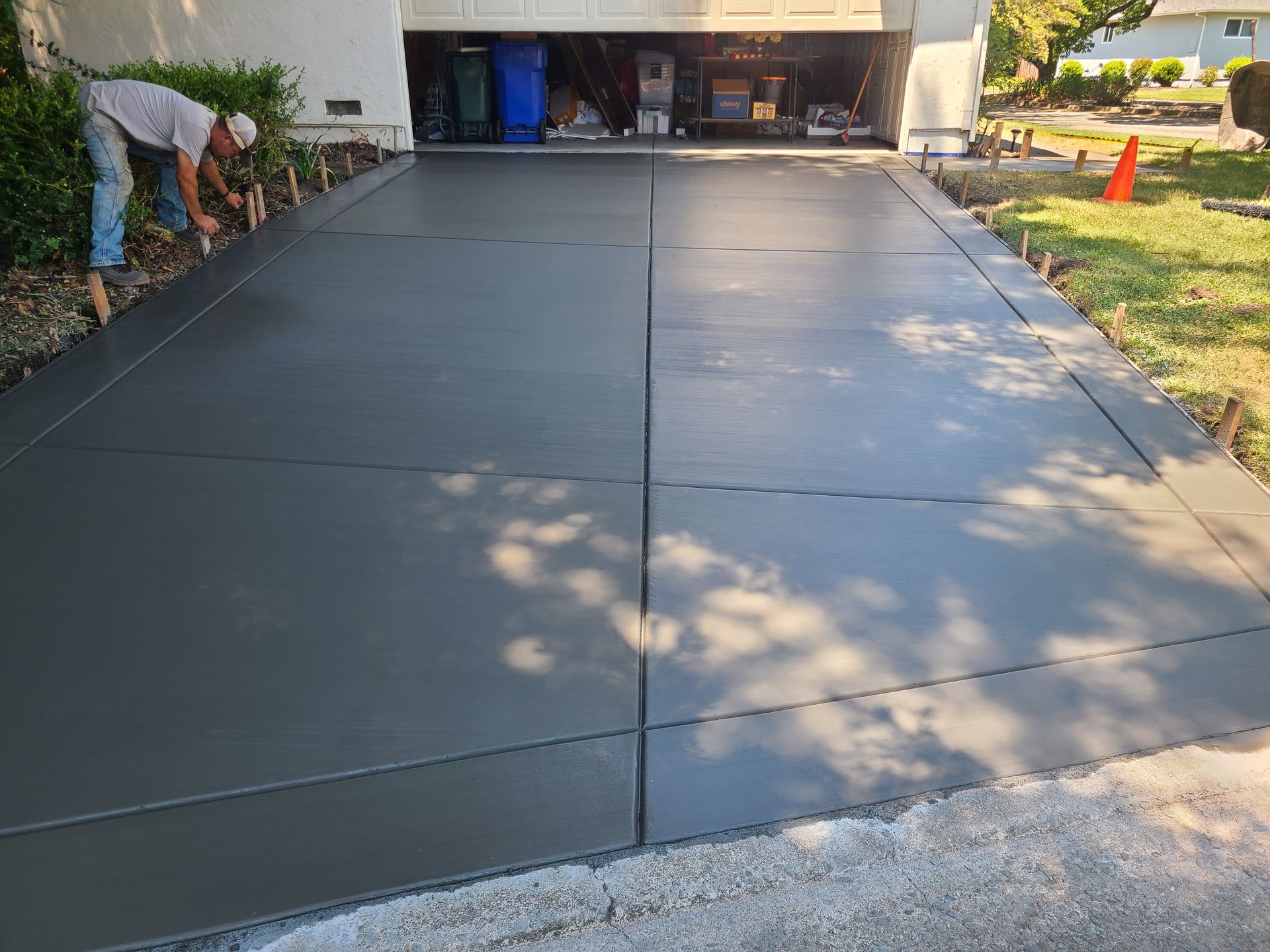 A man is working on a concrete driveway in front of a garage.