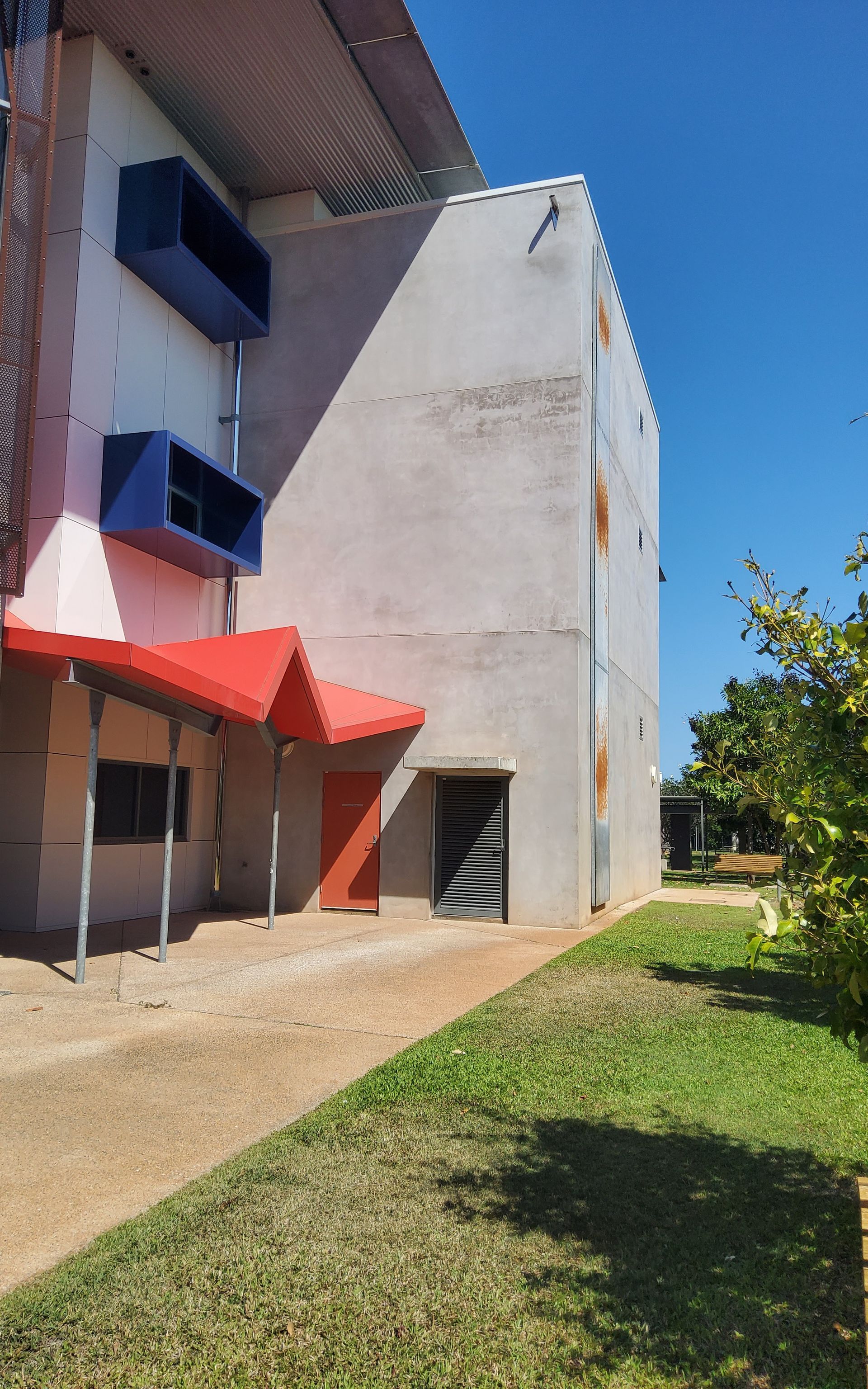 Side View of A Building with Blue Air Vents, Red Awning, and A Path with Grass on A Sunny Day — EXPOSURE NORTH PLASTERING PTY LTD in Berry Springs, NT