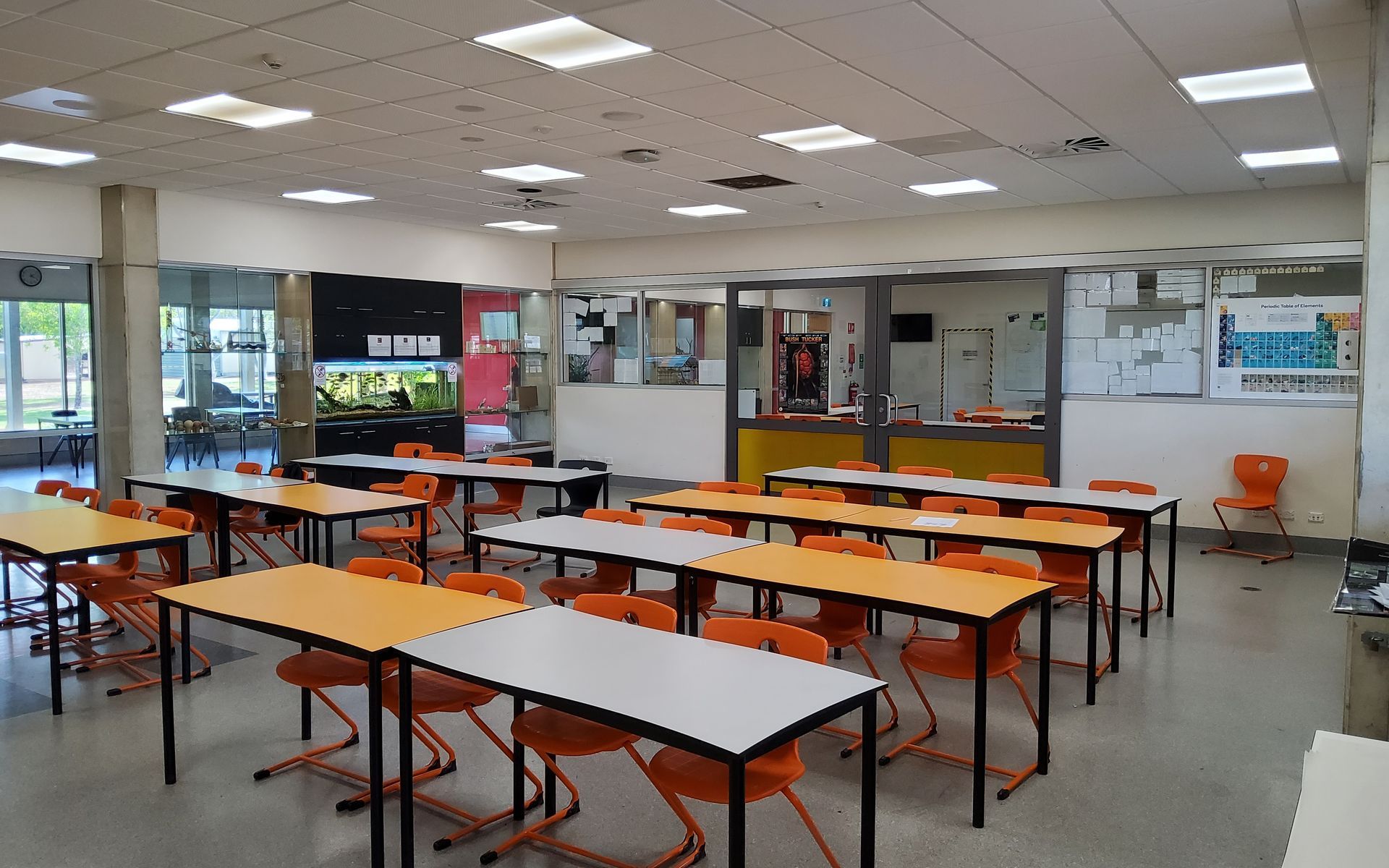 An Empty Classroom With Orange Chairs and Desks. a Black, Orange, and White Wall With a Window is at the Back — EXPOSURE NORTH PLASTERING PTY LTD in Berry Springs, NT