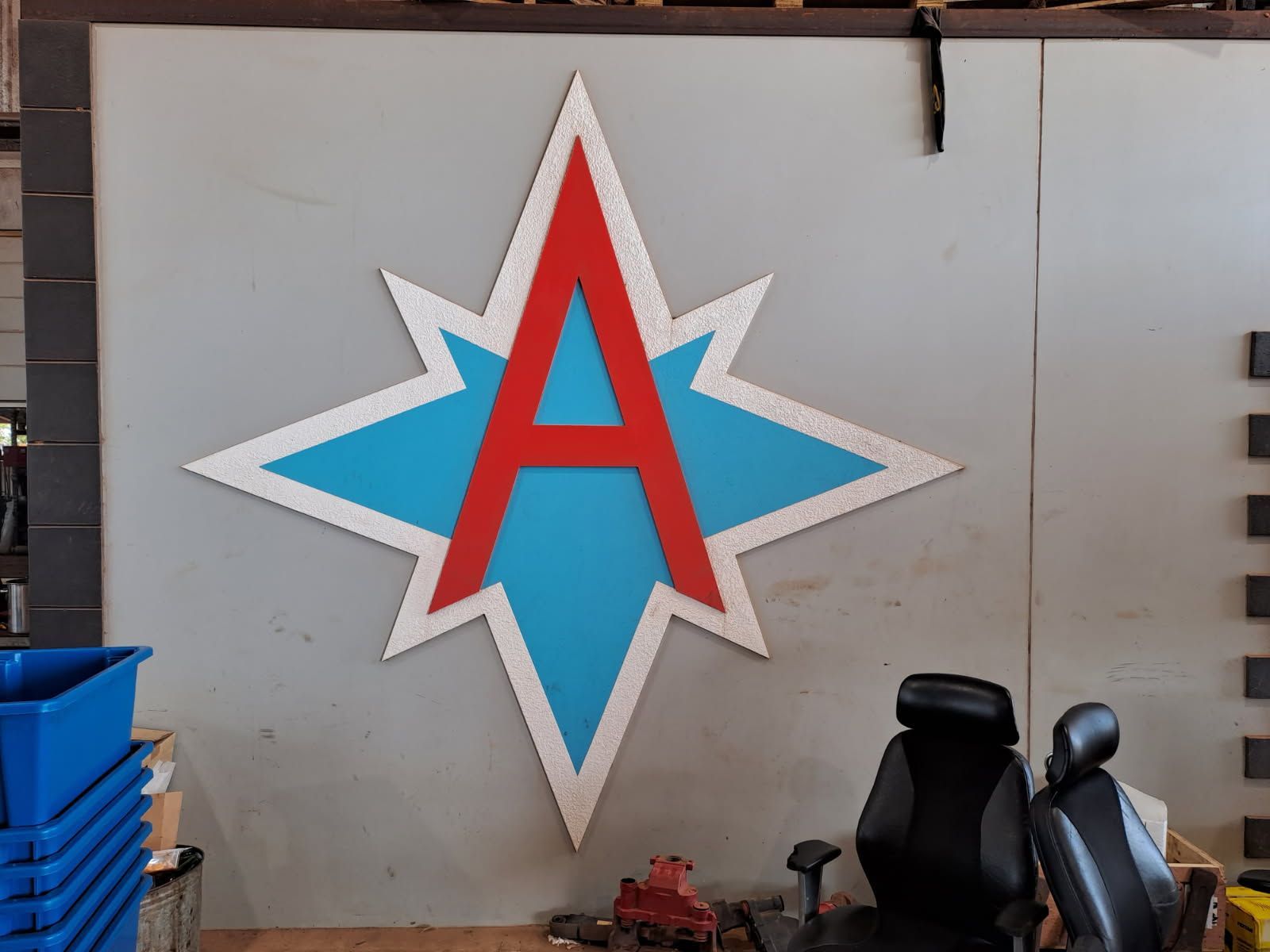 Large Red A Within a Blue Starburst on A Gray Wall, Above a Black Chair and Storage Containers — EXPOSURE NORTH PLASTERING PTY LTD in Berry Springs, NT