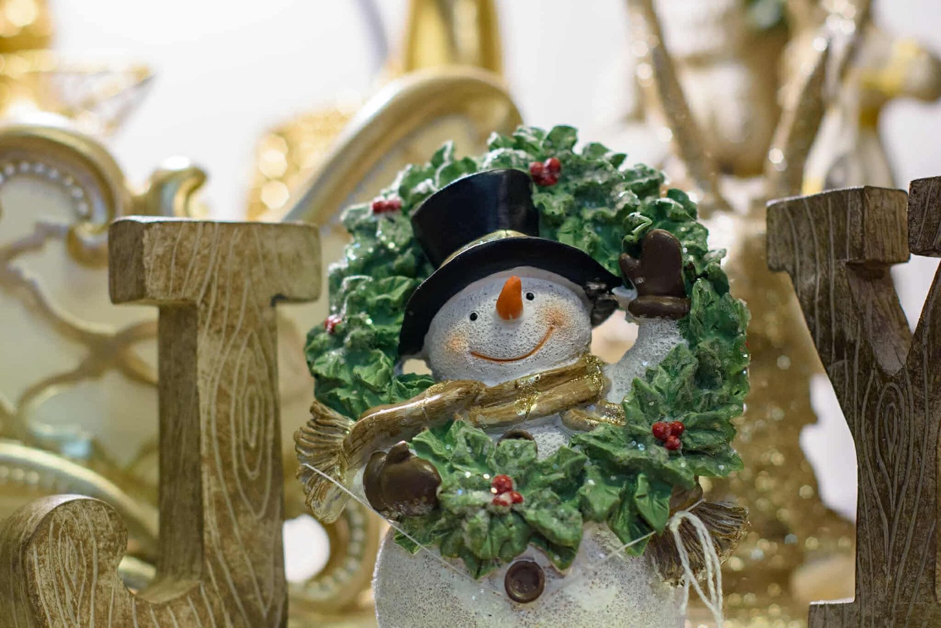 A snowman wearing a top hat and scarf is holding a wreath.