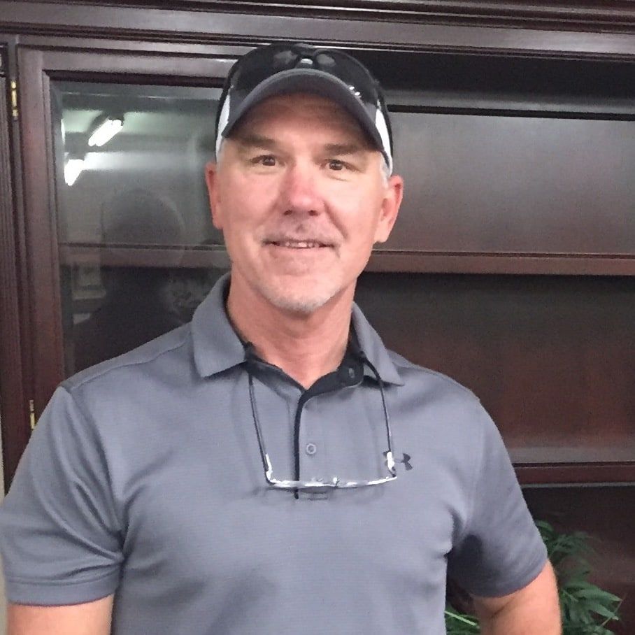 Man in gray polo and black cap smiling indoors in an office setting