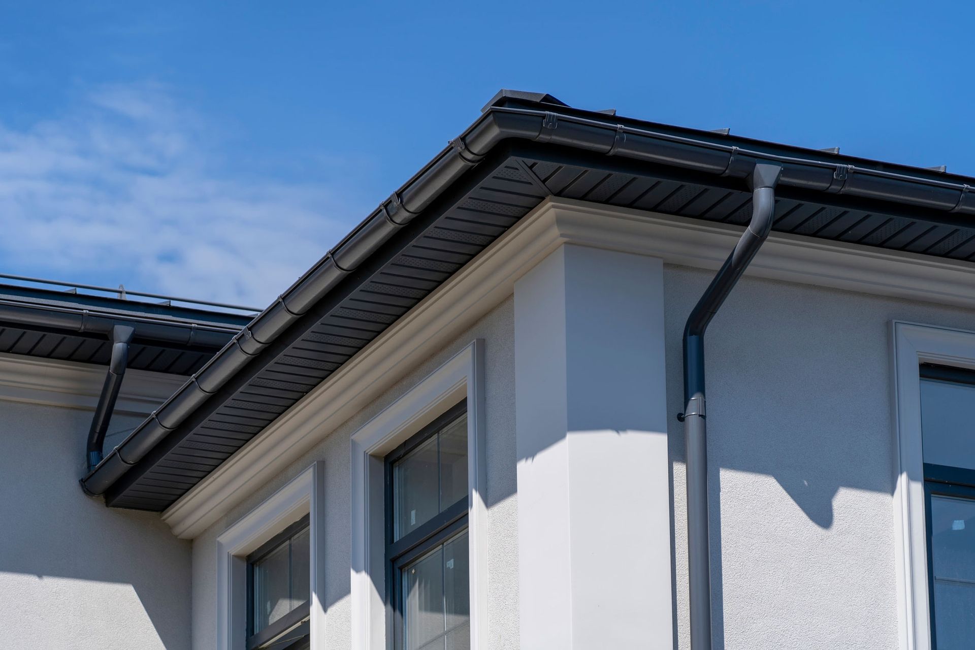 Black gutters on a white building's corner, with a blue sky in the background.
