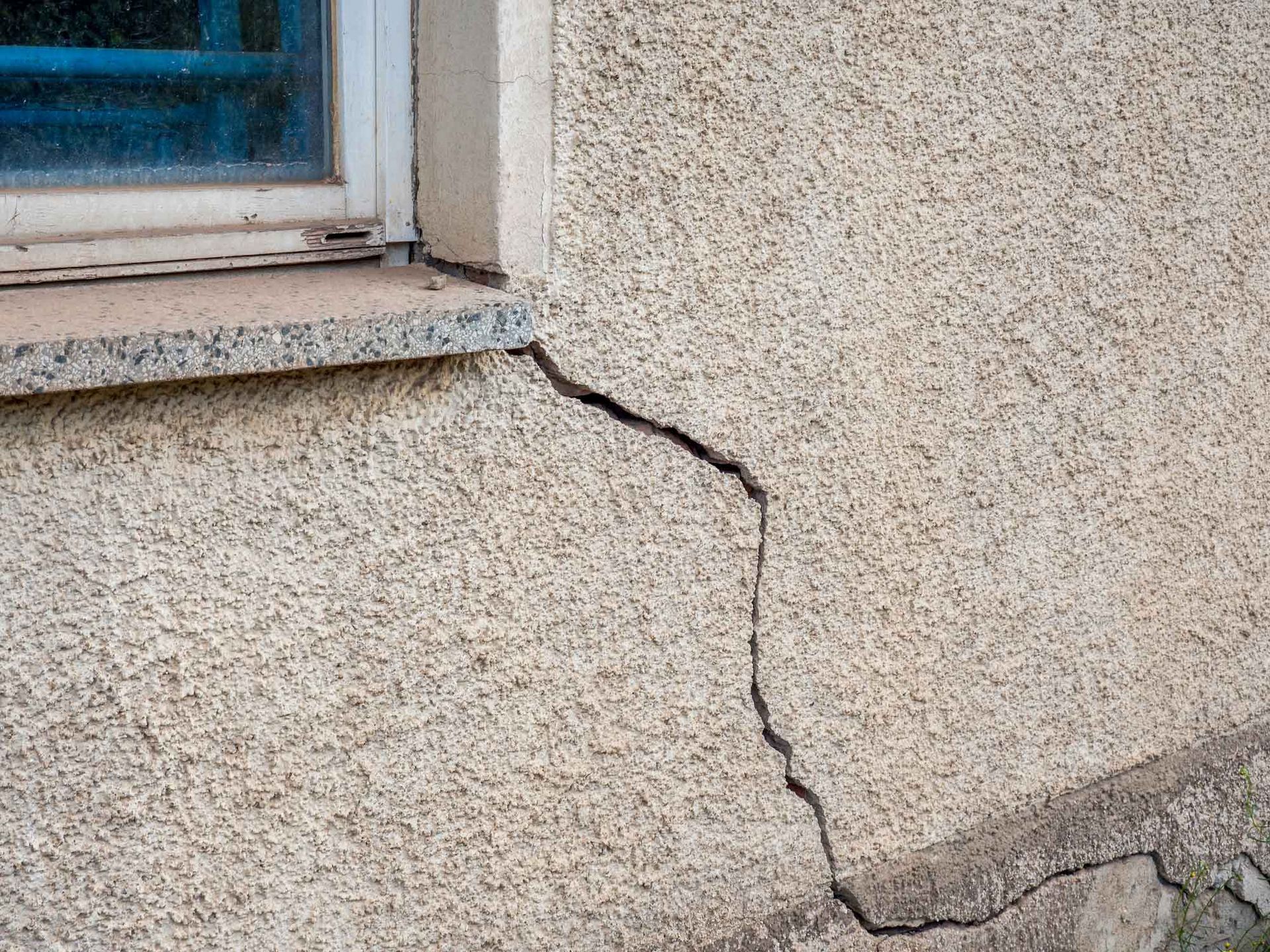 Cracked stucco wall near a window. 