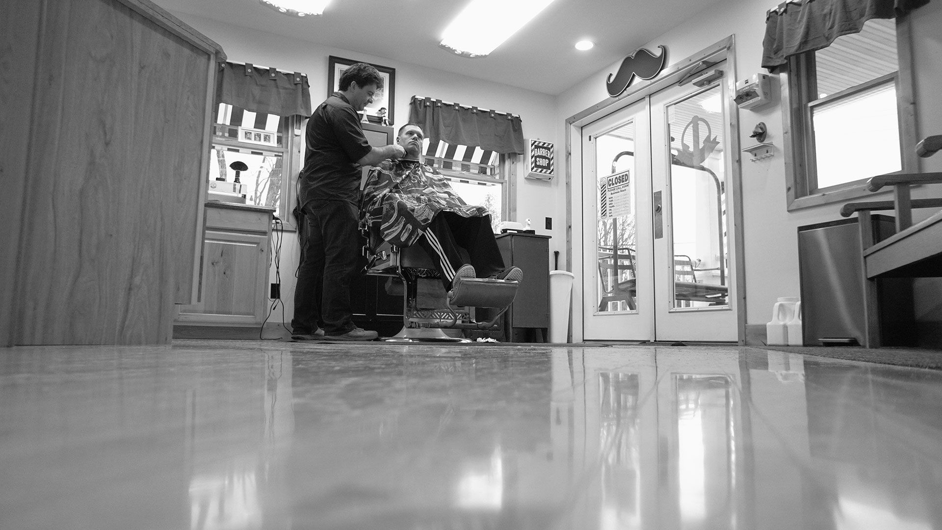 A wide perspective black and white photo of a traditional barbershop with a man sitting in a barber chair.