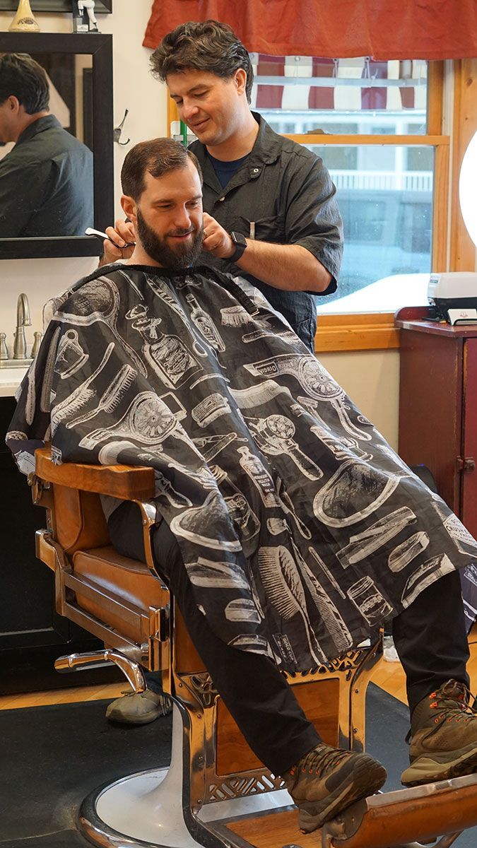 A barber and his customer engage in humorous conversation while the customer receives a neck trim with a straight razor.