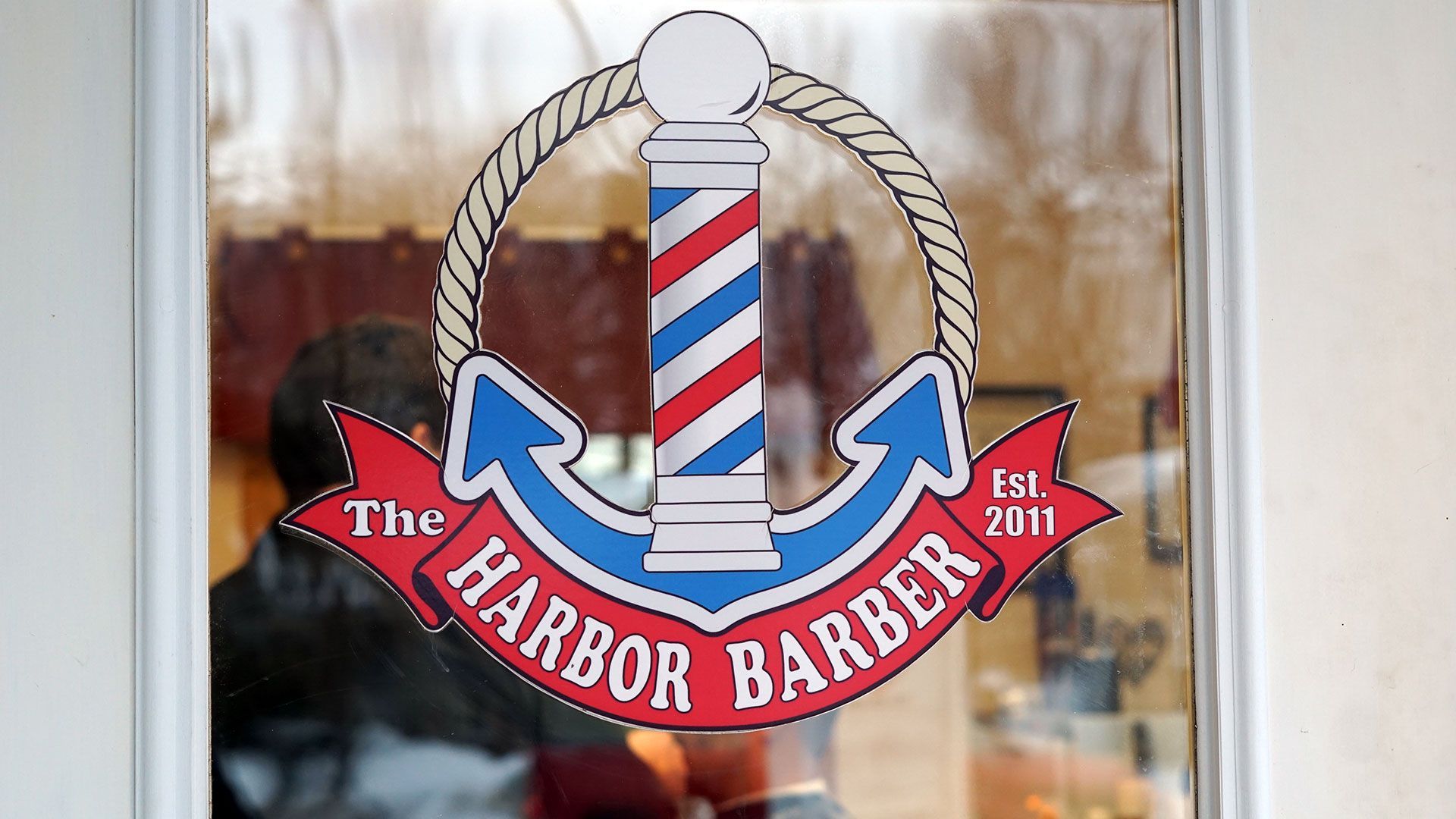 The front entry door to a traditional small-town barbershop with a logo decal that reads