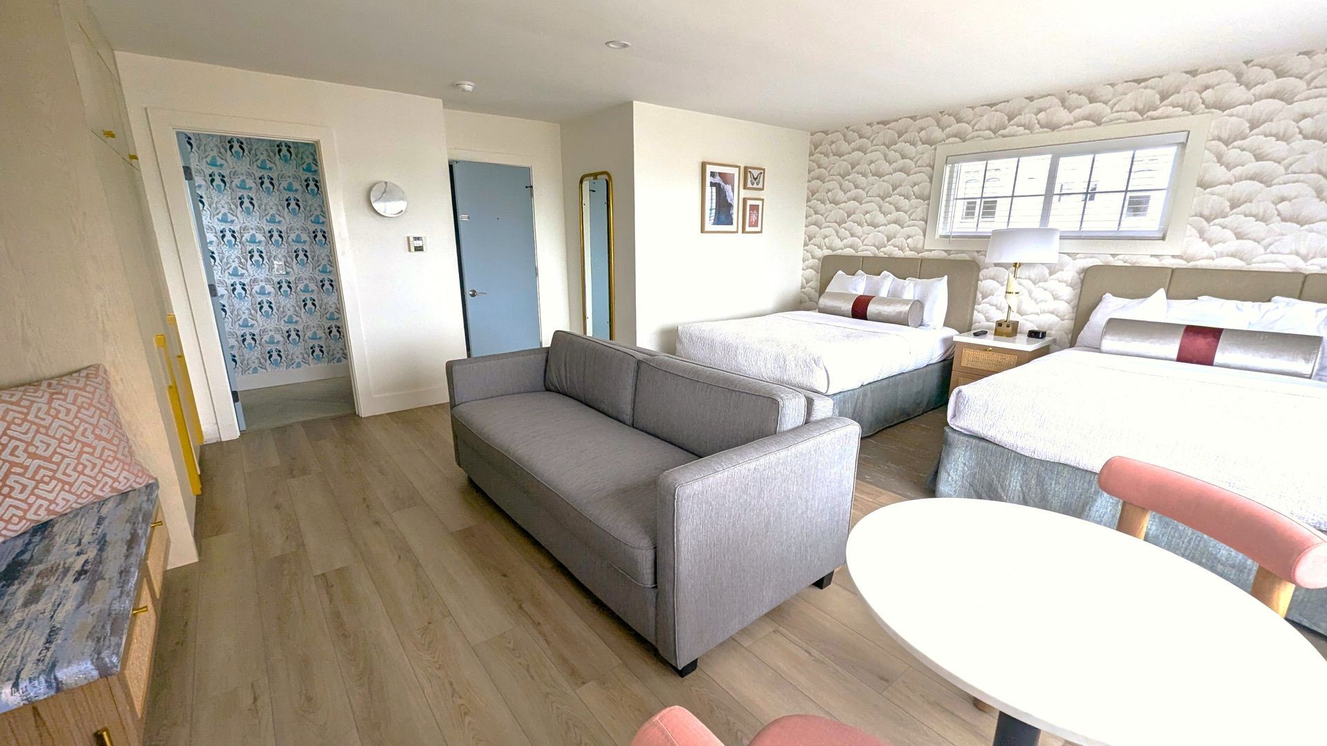 Couch next to a table in front of beds and two doors, one open and one closed 
