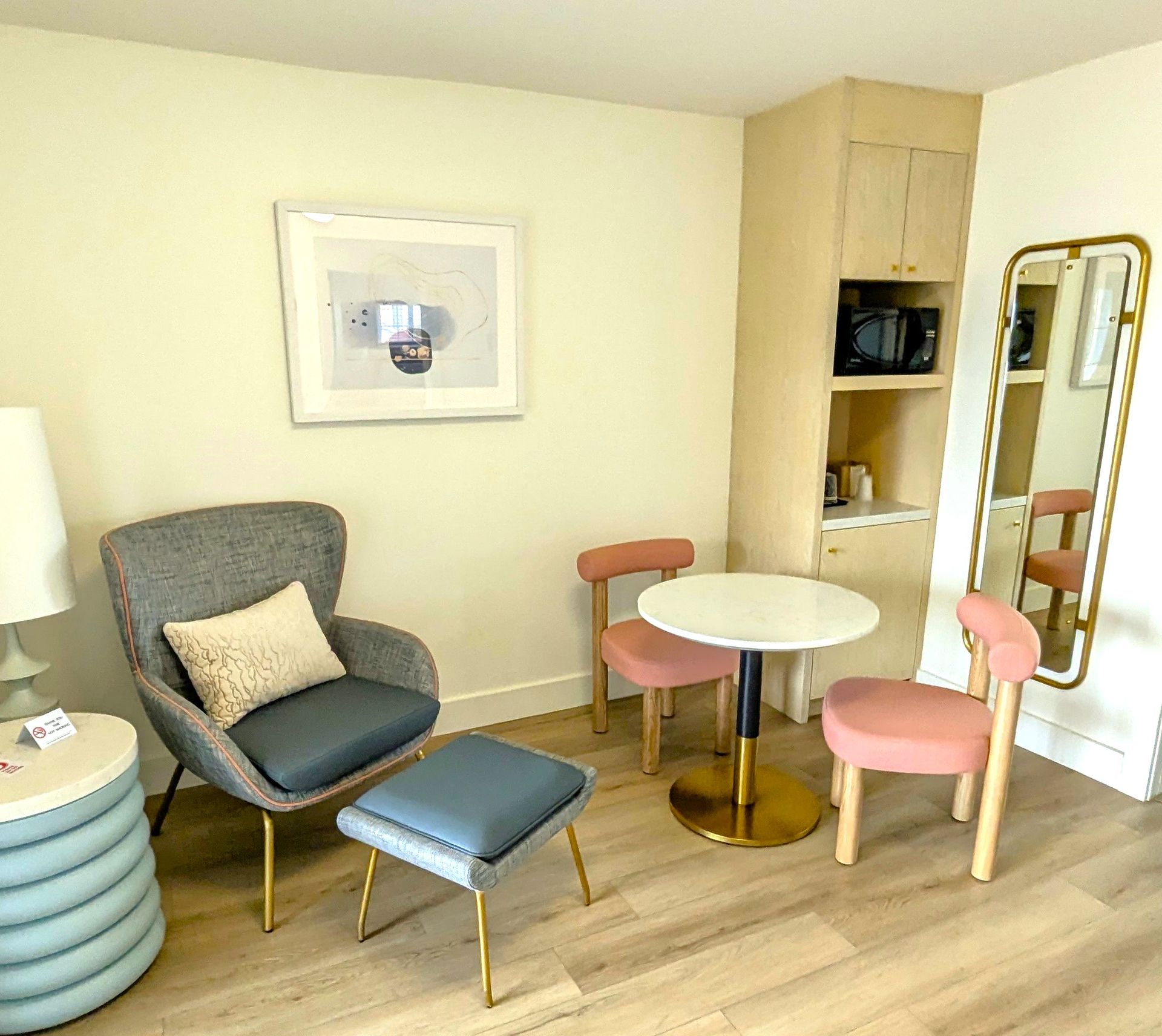 Room with a chair and ottoman, cabinet, mirror, table and chairs.