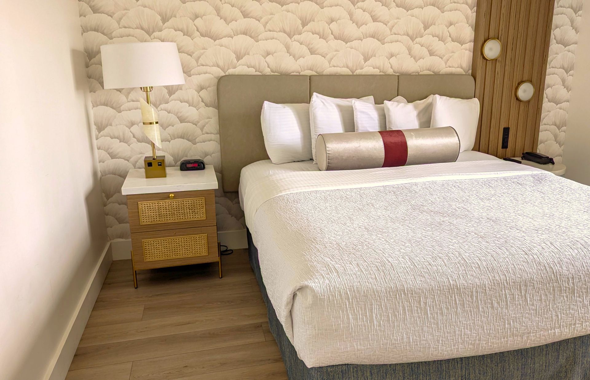 A nightstand with two drawers, a lamp, and a clock next to a bed.