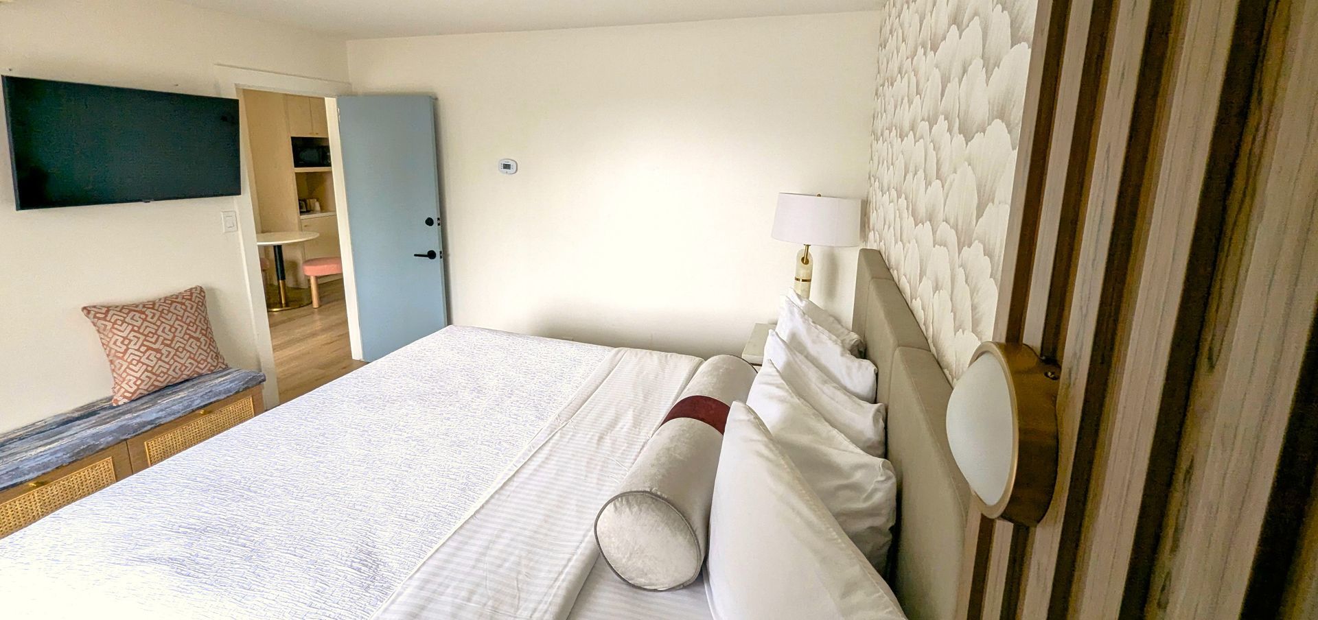 Bed in  a room with a TV, bench and door open into another room.