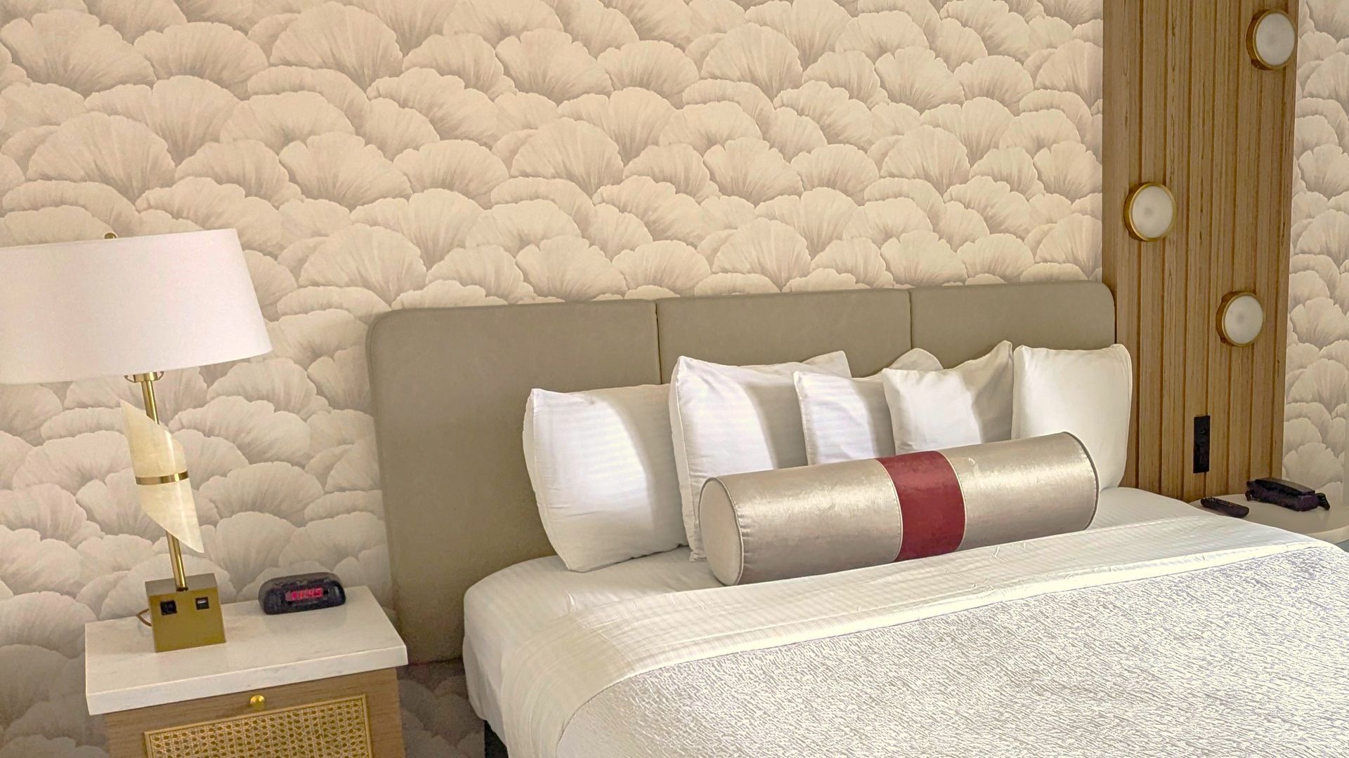 Bed with five pillows next to a nightstand with a lamp and clock on it.
