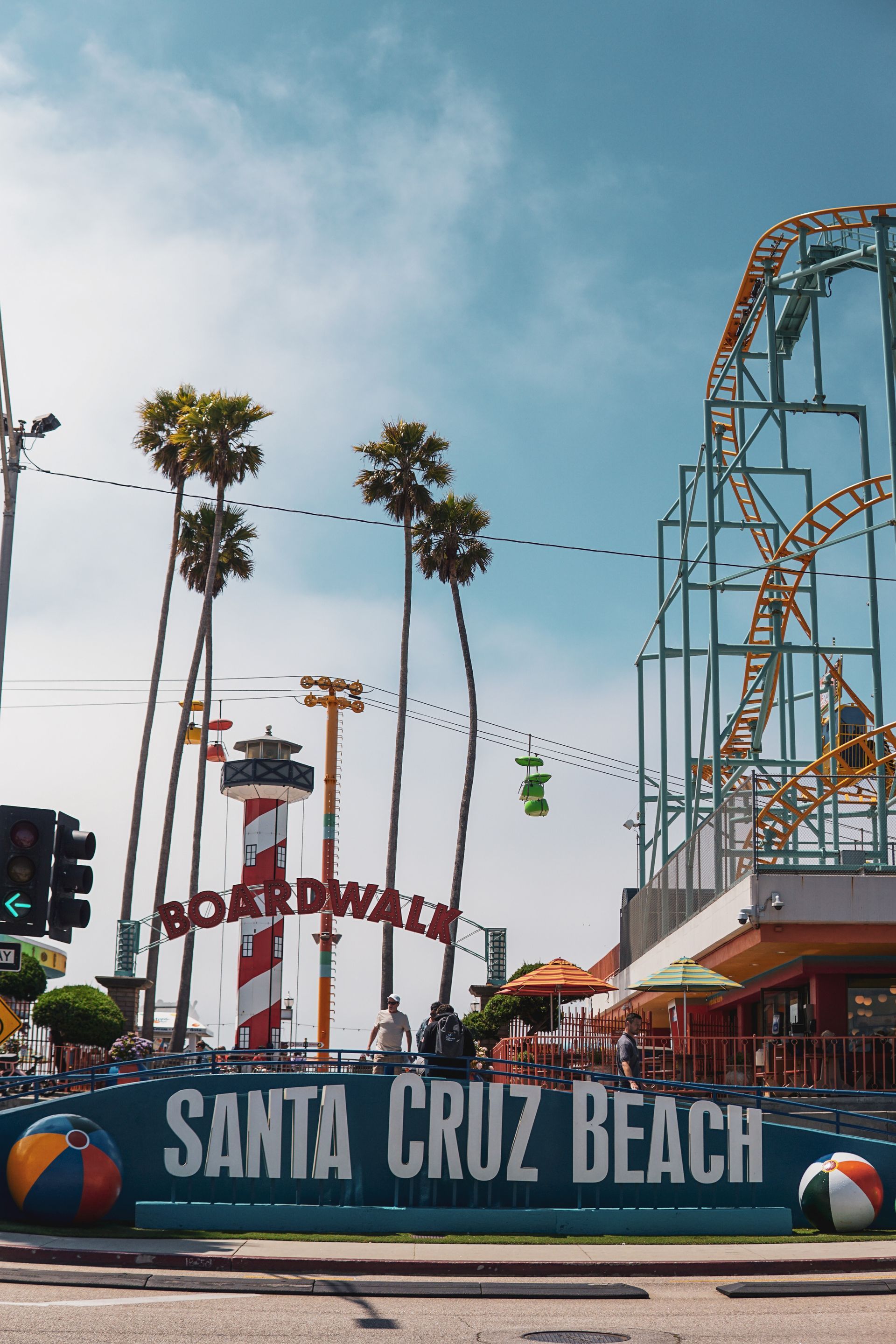 Santa Cruz Beach Boardwalk with palm trees, a red and white lighthouse shaped ride, and section of a roller coaster ride.