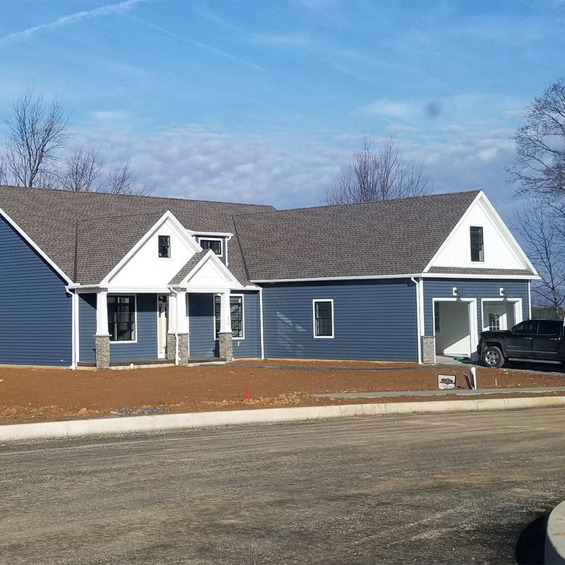 A new house with blue siding, a dark shingled roof, and white trim under a clear blue sky, with a truck parked in front.