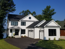 A modern, two-story white house with a dark roof and black window frames, featuring an attached garage and front porch.