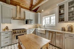 A bright kitchen features gray cabinetry, a central wooden island, stainless steel appliances, and a tiled floor.
