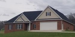 A red brick, one-story suburban home with a multi-gabled roof, white garage door, and light siding, set in a grassy yard.