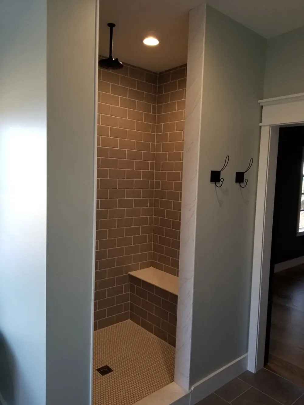 A walk-in shower with brown subway tile walls, a built-in stone bench, and a rainfall showerhead in a light-walled room.