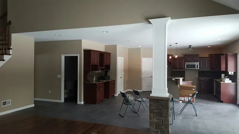 An open-concept living area with dark cabinetry, gray tiled floors, and a stone-based white column in the center.