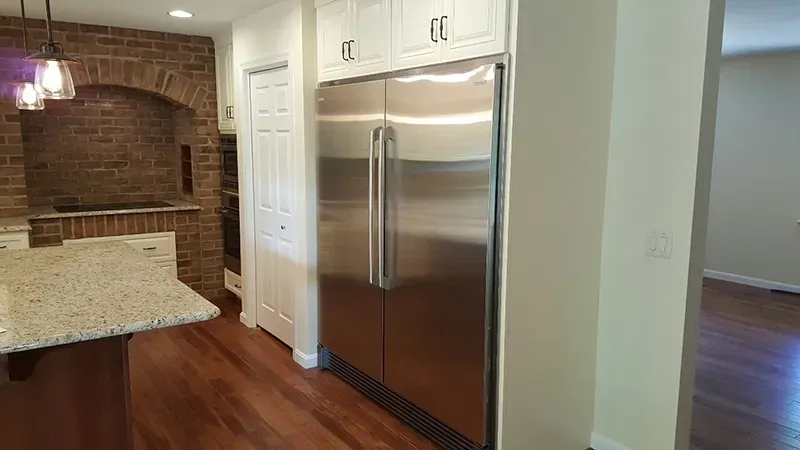 A modern kitchen featuring a stainless steel refrigerator, white cabinets, and a brick accent wall with arched shelving.
